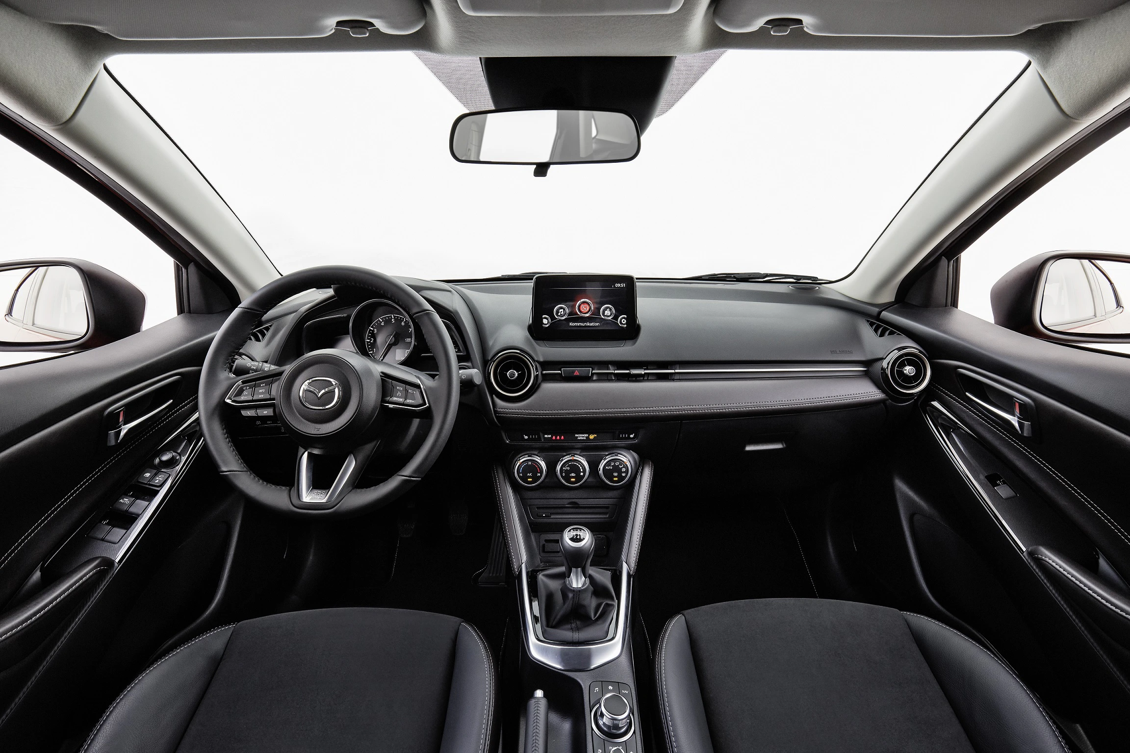Innenraum eines Autos mit schwarzer Ausstattung, Lenkrad links, zentralem Display und Bedienungsreglern auf der Mittelkonsole.