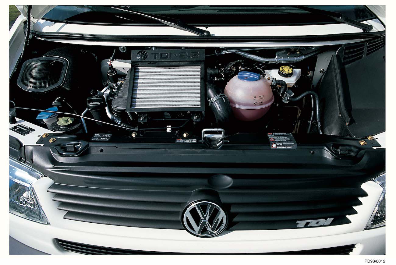 Motorraum eines VW TDI mit sichtbarem Kühler, Batterie und Kühlmittelbehälter. Markantes VW-Logo auf schwarzem Kühlergrill.