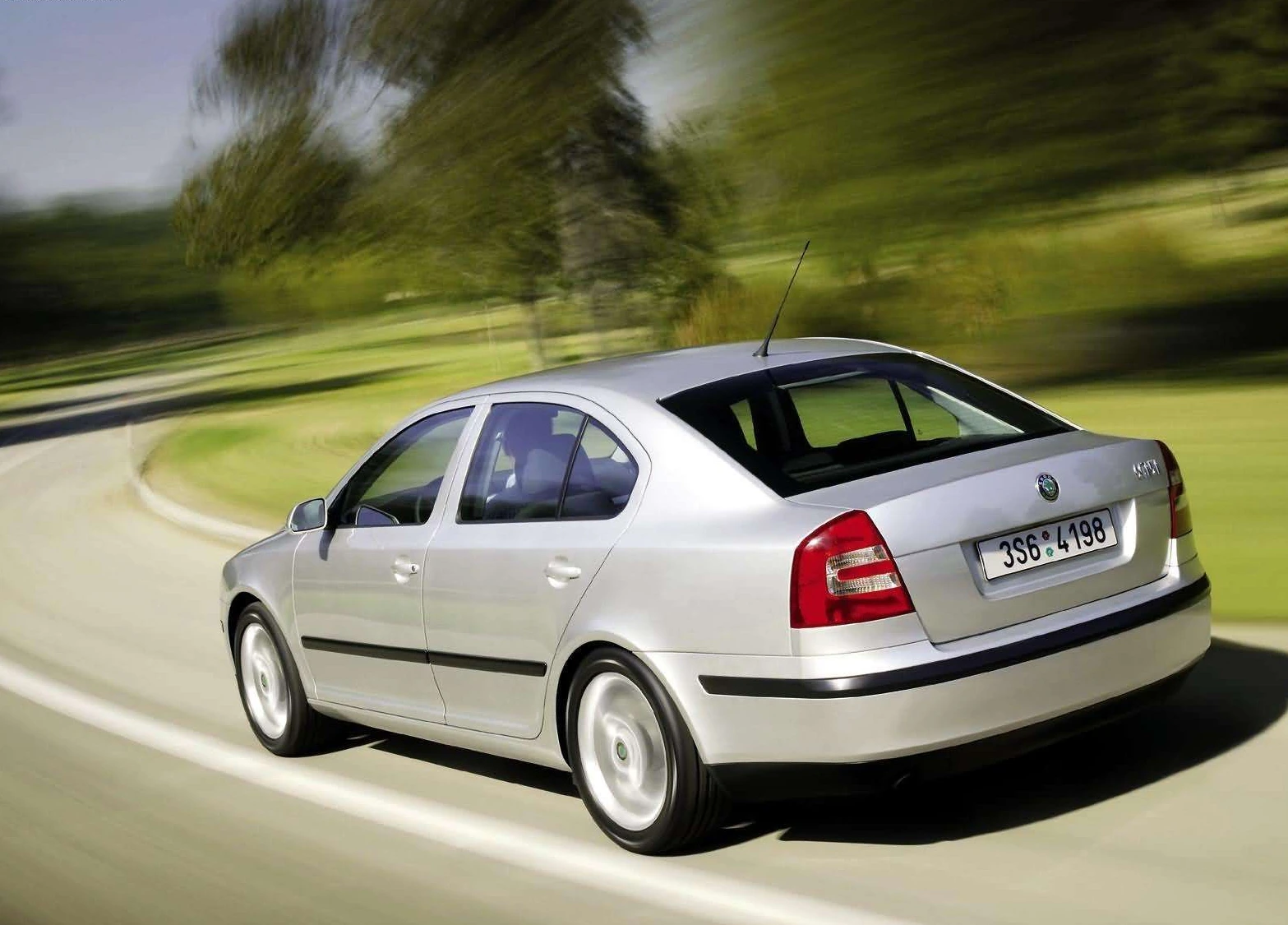 Silberner Skoda Octavia fährt dynamisch auf einer kurvigen Landstraße. Bäume und Wiese sind im Hintergrund verschwommen zu sehen.