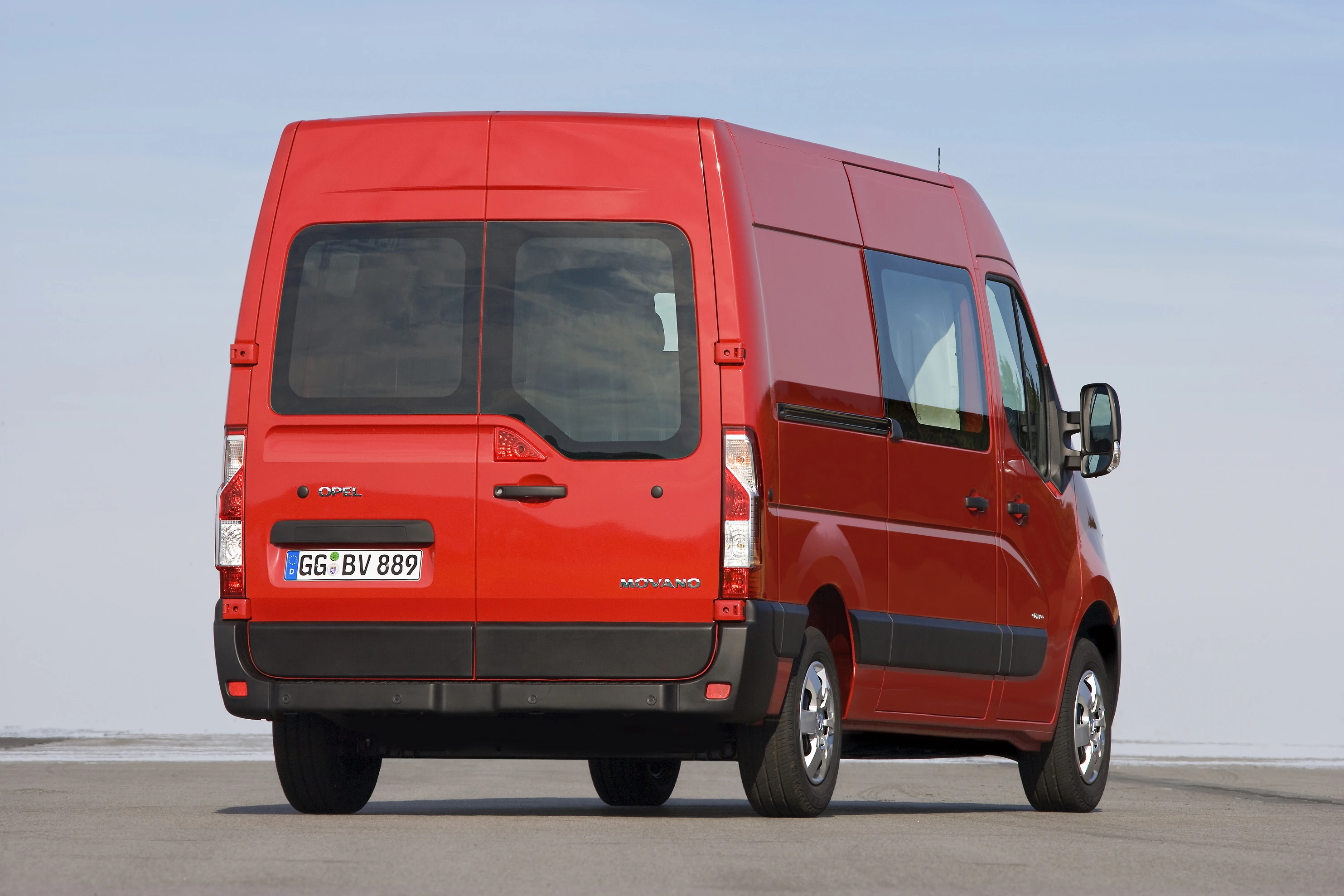 Roter Transporter von hinten auf einer Straße, breiter Himmel im Hintergrund.