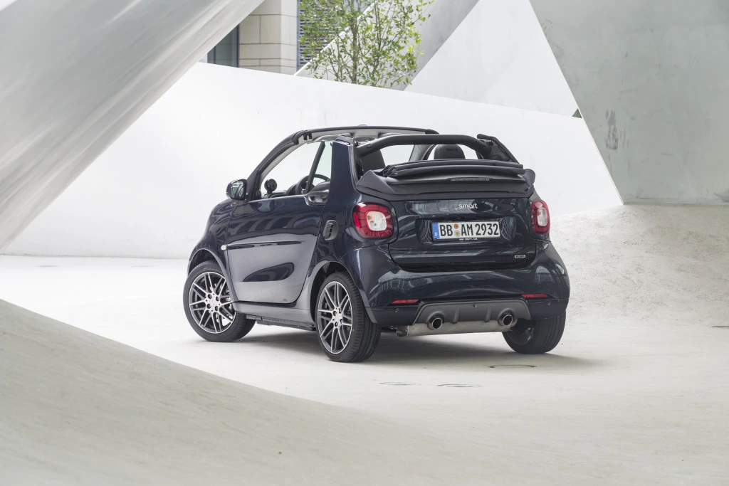 Schwarzer Smart Cabrio steht in einem modernen weißen architektonischen Umfeld. Fahrzeug von hinten betrachtet, klare Linien und sportliches Design.