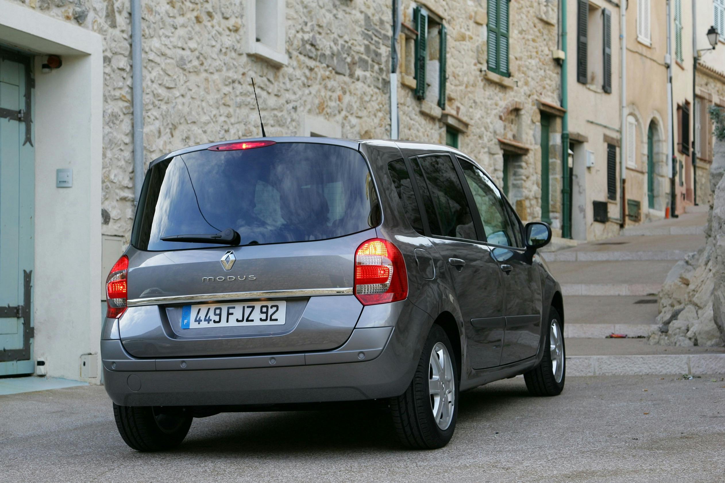 Grau-silberner Renault Modus parkt auf einer schmalen, gepflasterten Straße vor historischen Steingebäuden.