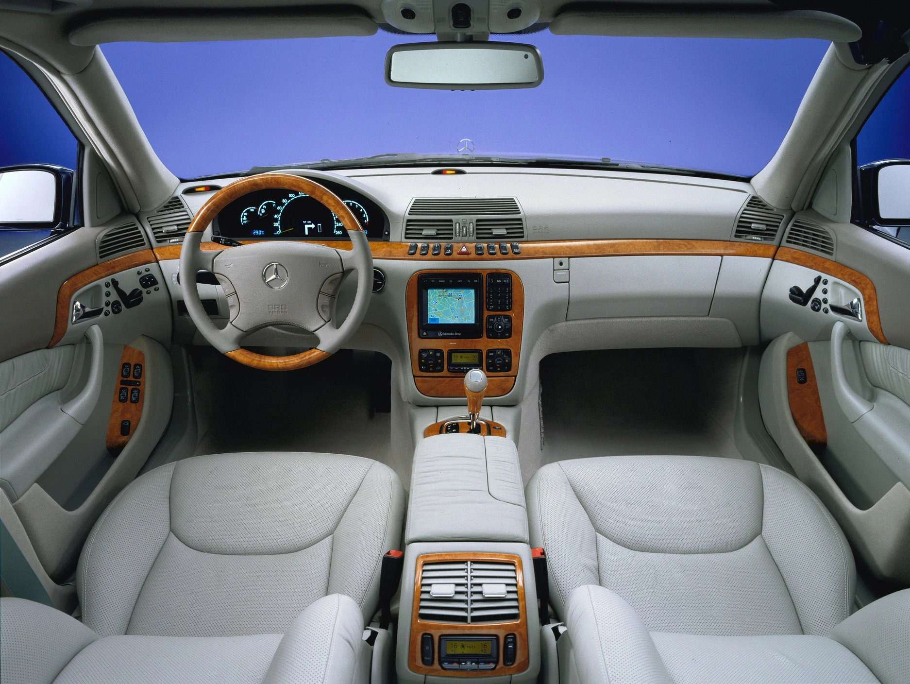 Innenraum eines Luxusautos mit beigen Ledersitzen, Holzverkleidung, Navigationssystem und klassischem Mercedes-Lenkrad.