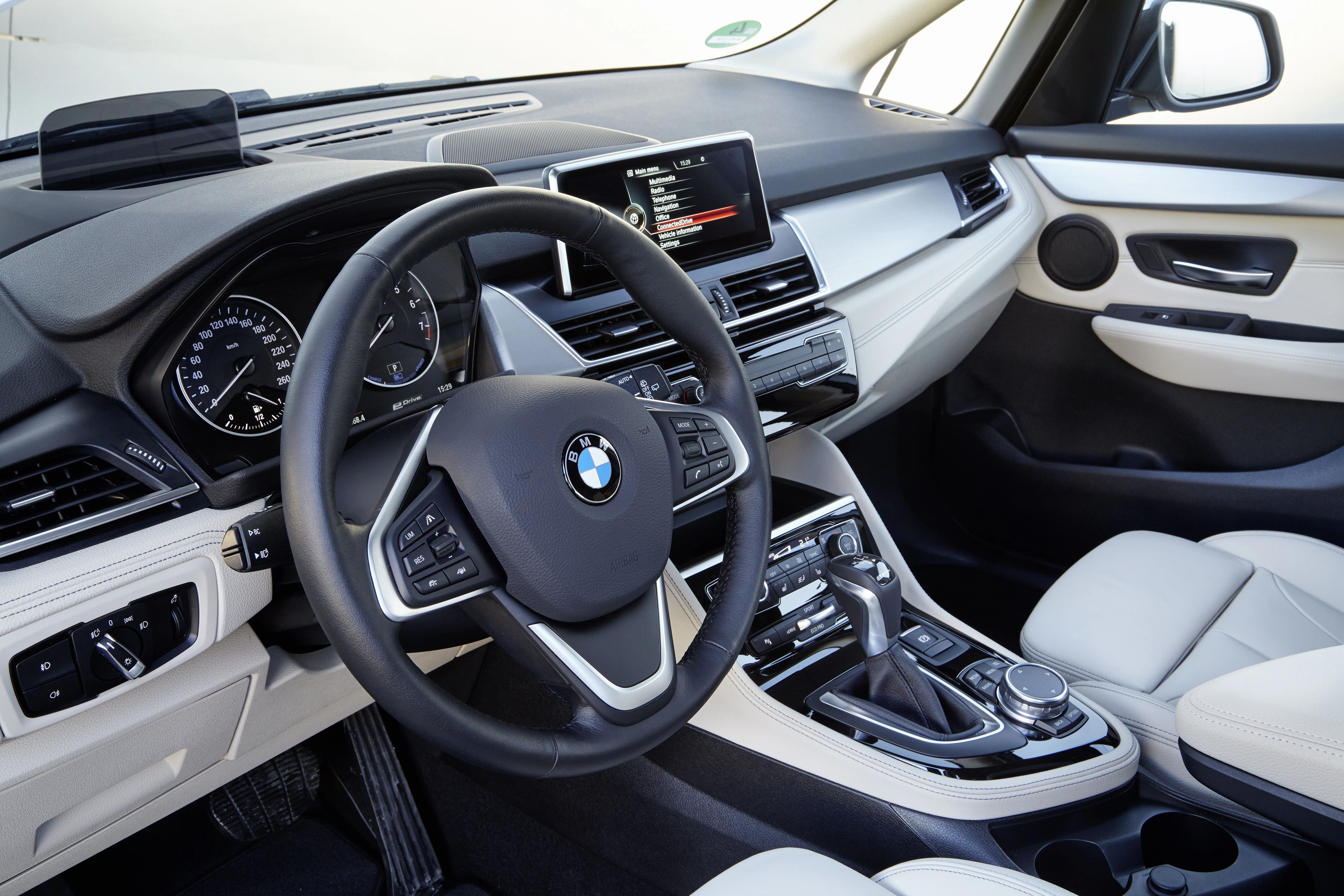 Innenraum eines BMW mit schwarzem Lenkrad, modernem Armaturenbrett und hellem Lederinterieur. Das Navigationsdisplay ist eingeschaltet.