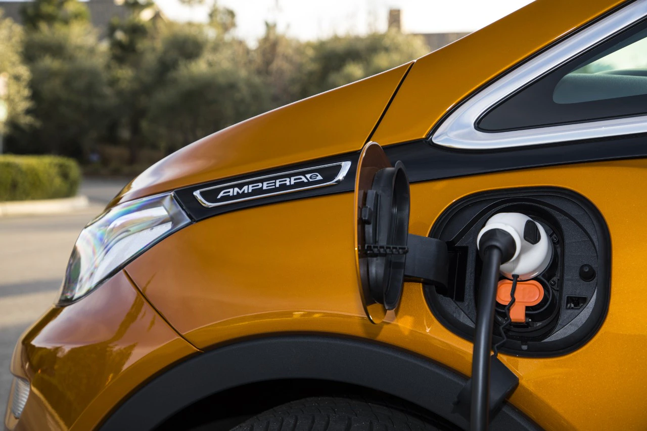 Orangefarbenes Elektroauto wird aufgeladen. Ladeanschluss ist geöffnet, Kabel angeschlossen. Umfeld unscharf im Hintergrund.
