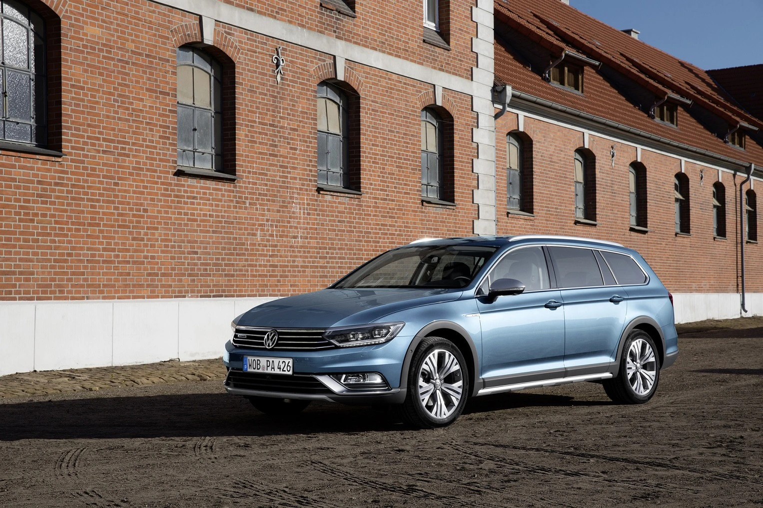 Blauer Volkswagen Passat Kombi parkt vor einem Gebäude mit roten Backsteinen und mehreren Fenstern.