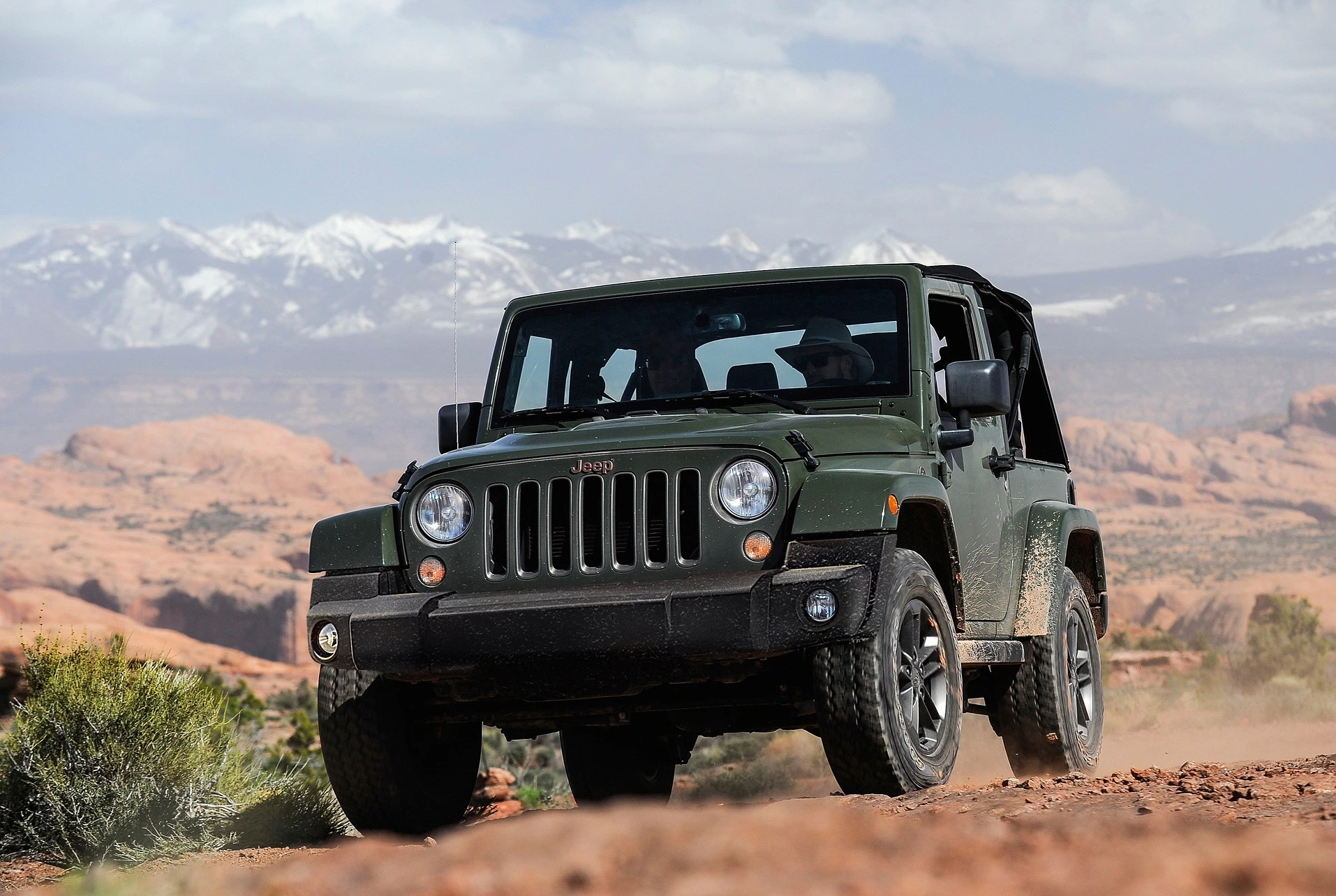 Ein grüner Jeep fährt auf einer staubigen Offroad-Strecke in einer Wüstenlandschaft mit Bergen im Hintergrund.