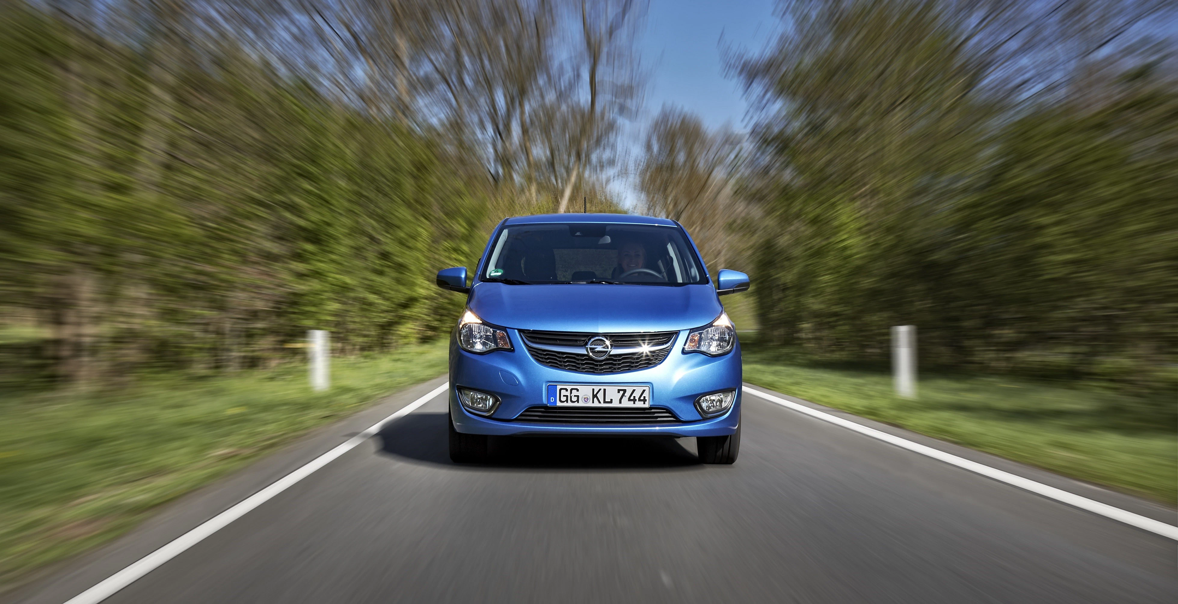 Blauer Opel-Familienwagen fährt auf einer Landstraße. Verschwommener Hintergrund deutet auf Geschwindigkeit hin. Grünen Bäume säumen die Straße.