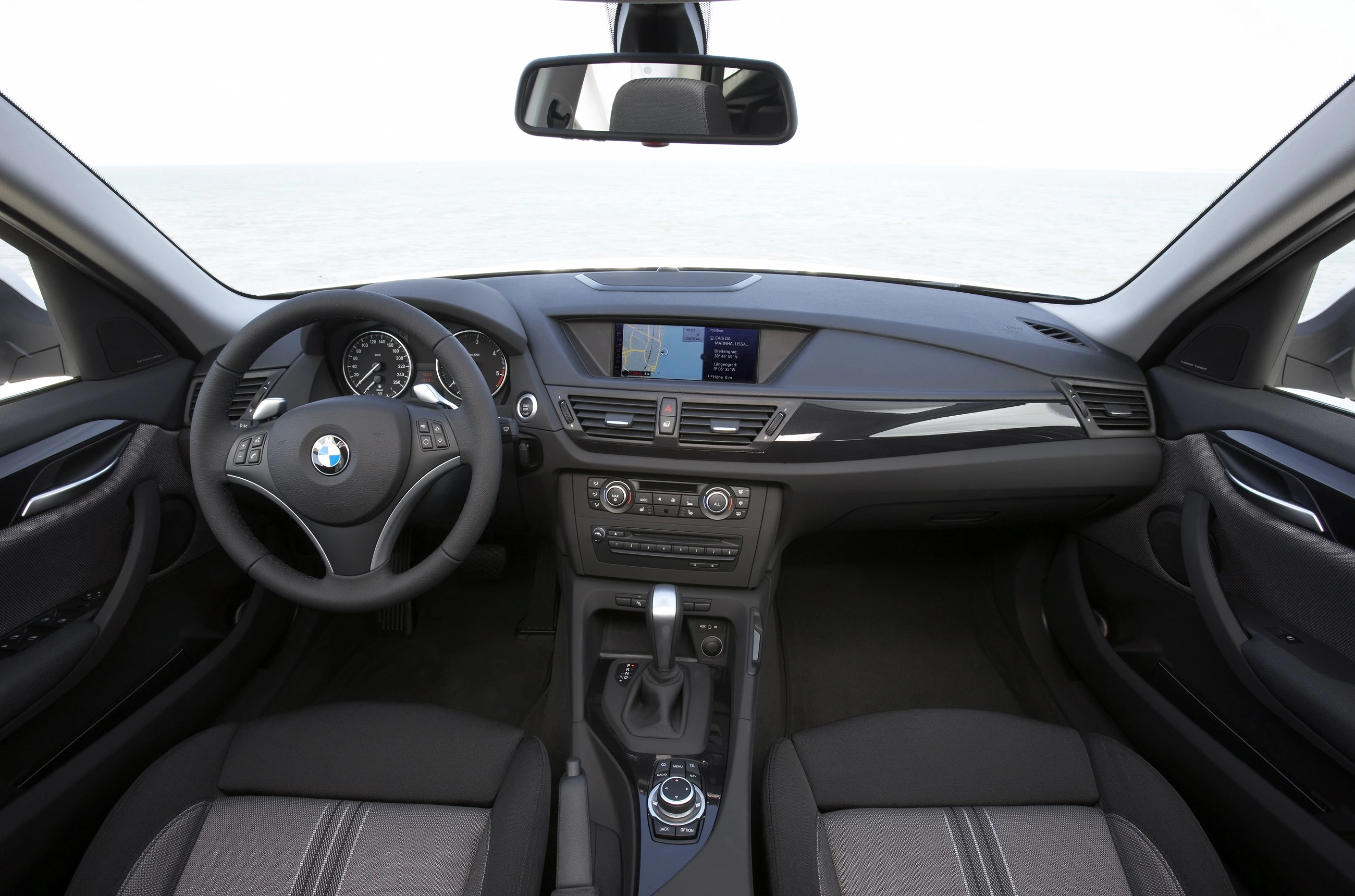 Innenraum eines BMW-Autos mit modernem Lenkrad und Armaturenbrett, zentralem Bildschirm und schwarzen Sitzen.