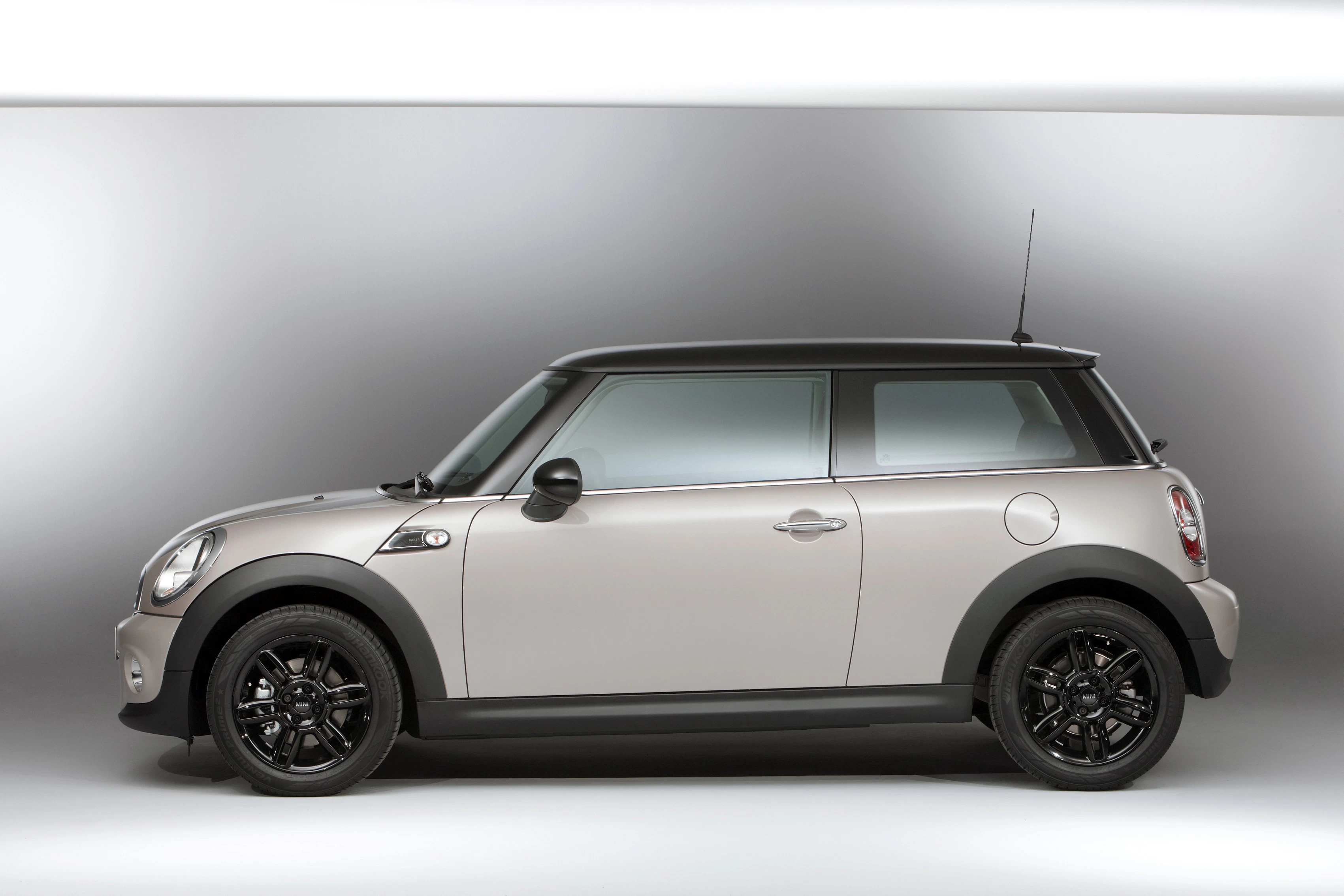 Silberner Mini Cooper in Seitenansicht, statisch im Fotostudio. Elegantes Design mit schwarzem Dach und schwarzen Felgen.