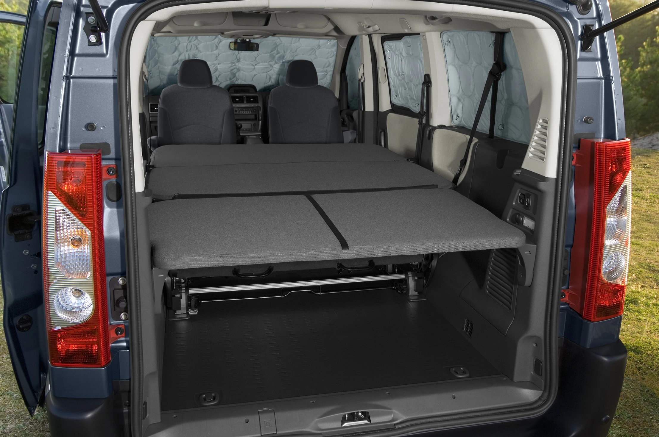 Innenraum eines umgebauten Vans mit zwei ausgeklappten Schlafplätzen, Blick durch die geöffnete Heckklappe.