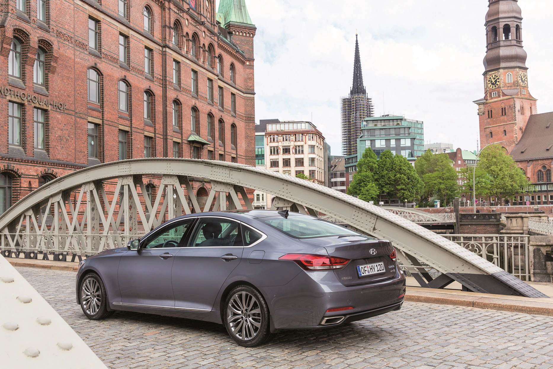 Limousine auf einer Brücke in Hamburg mit historischen Gebäuden im Hintergrund, darunter ein Kirchturm und ein grünes Gebäude.