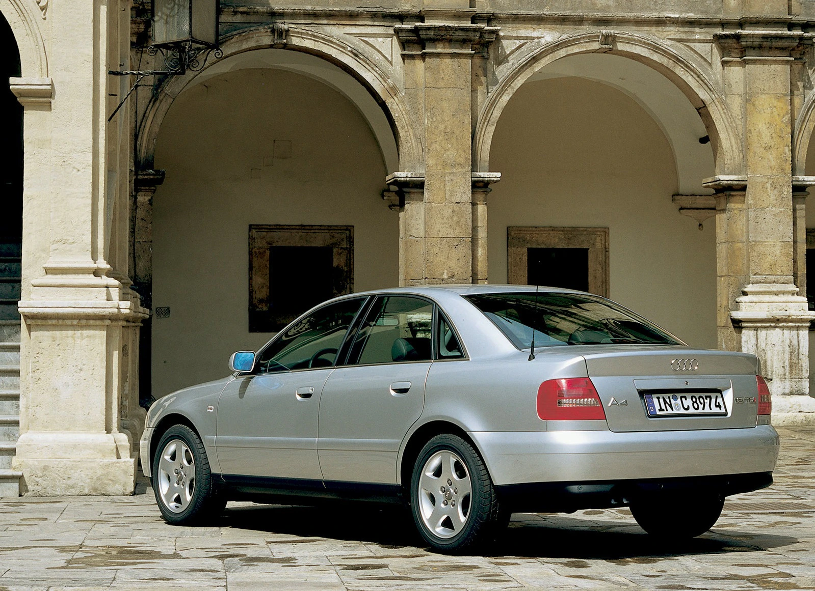 Silberner Audi Limousine parkt auf einem historischen Pflasterplatz vor einem Gebäude mit Rundbogenarkaden.
