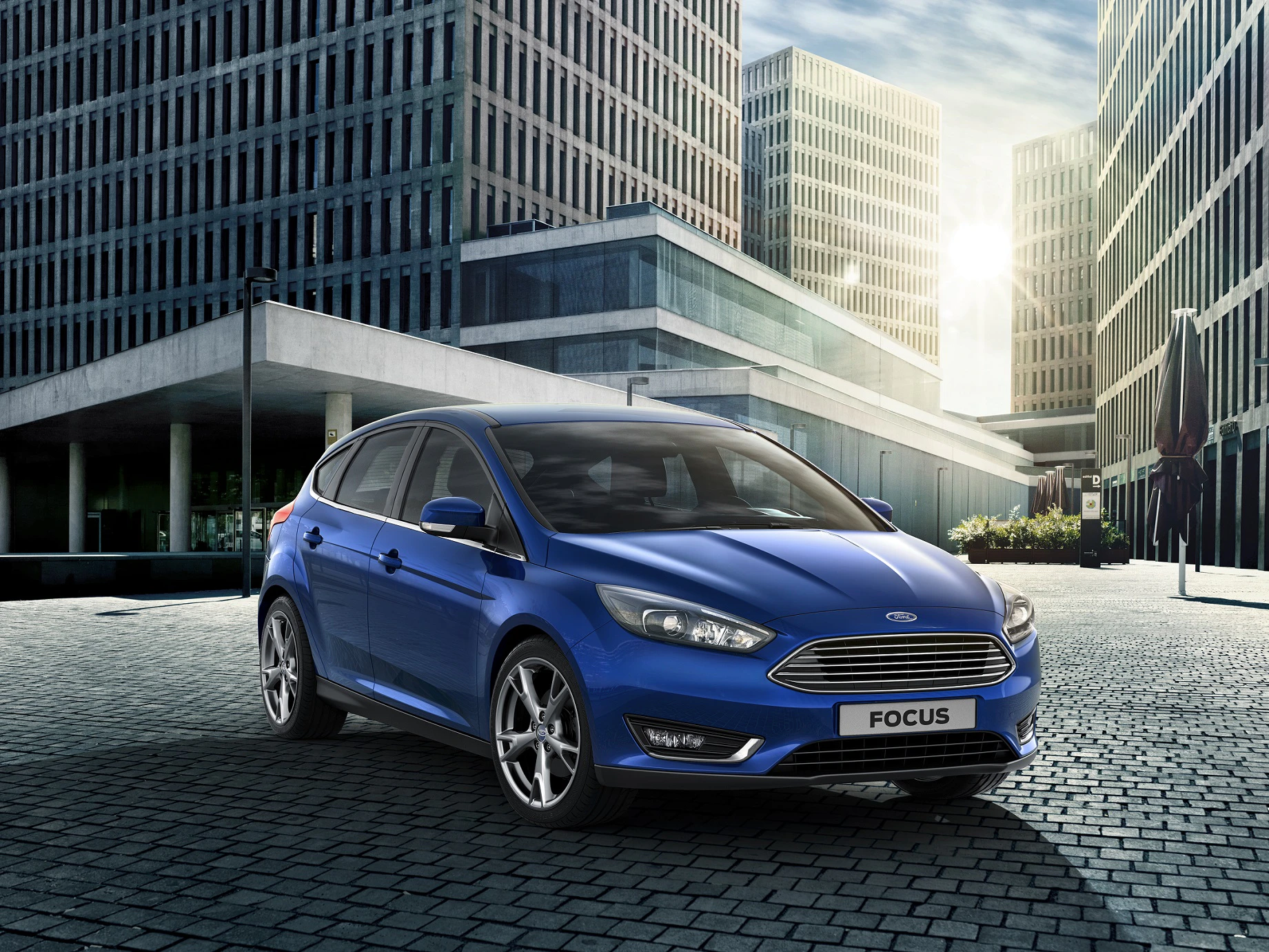 Blauer Ford Focus in modernem, urbanem Umfeld mit hohen Gebäuden und Pflastersteinstraße bei sonnigem Wetter.