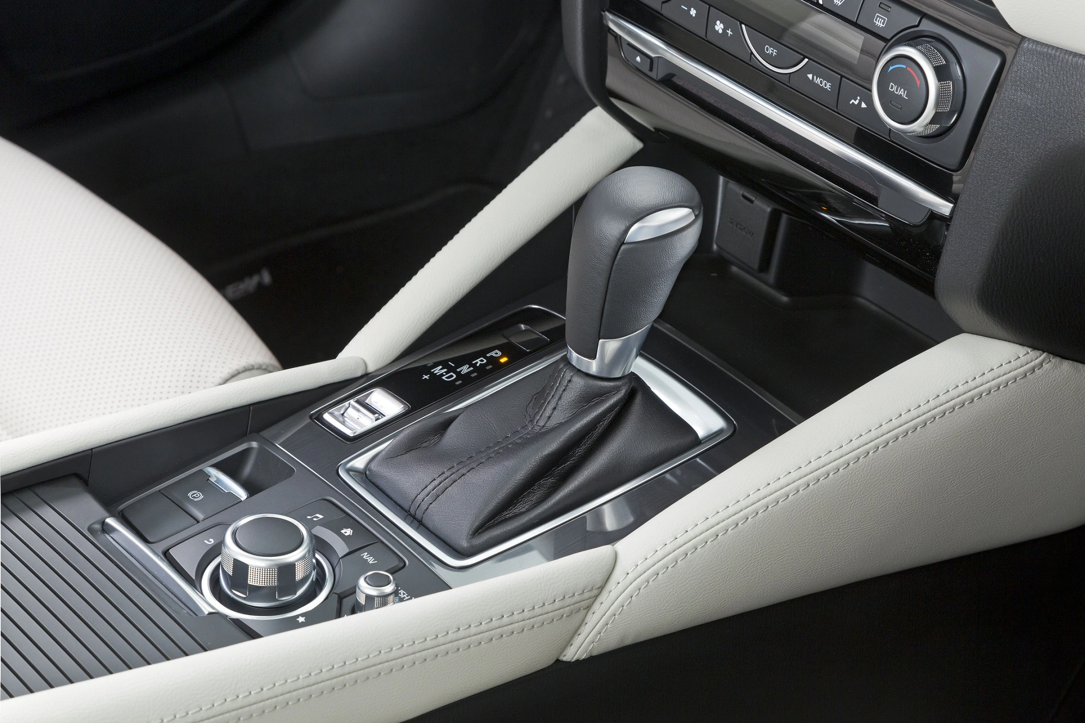Nahaufnahme einer Automatik-Gangschaltung in einem modernen Auto, umgeben von cremefarbenem Leder und Bedienelementen auf der Mittelkonsole.