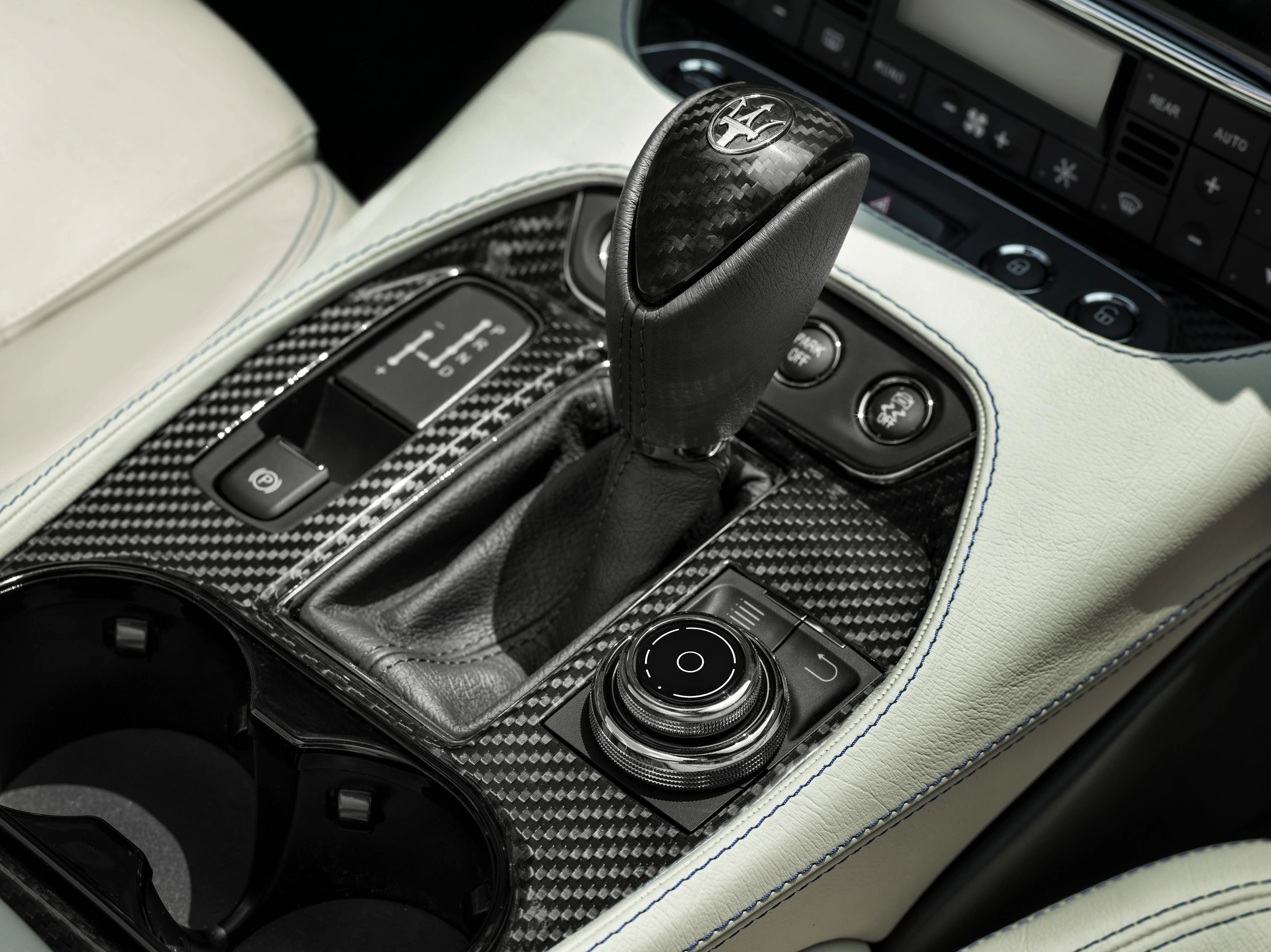 Nahaufnahme eines luxuriösen Autoinnenraums mit einem Schalthebel aus Karbonfaser, umgeben von Bedienelementen und heller Lederverkleidung.