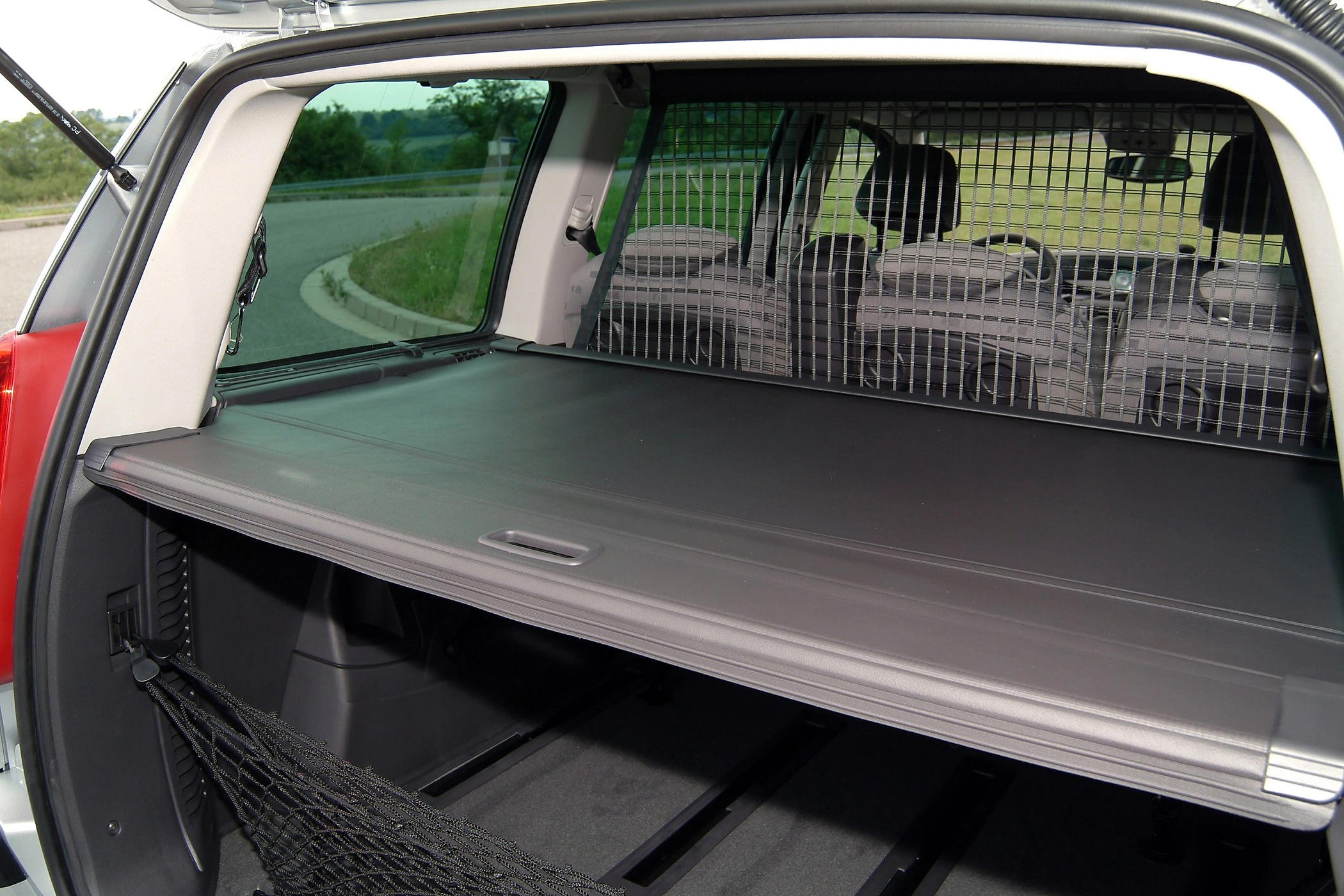 Kofferraum eines Autos mit Laderaumabdeckung, Hundeschutzgitter und aufgerolltem Netz für sicheren Transport von Gepäck oder Tieren.