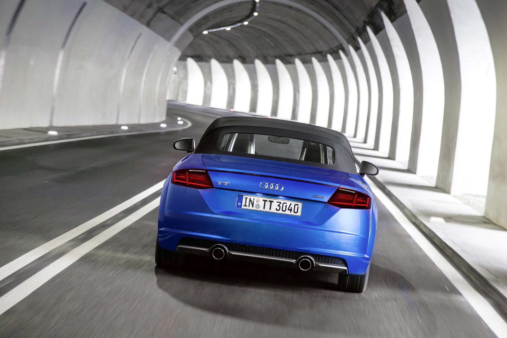 Blauer Audi TT fährt durch einen modernen, beleuchteten Tunnel. Sicht von hinten, Betonwände und Lichtstreifen.