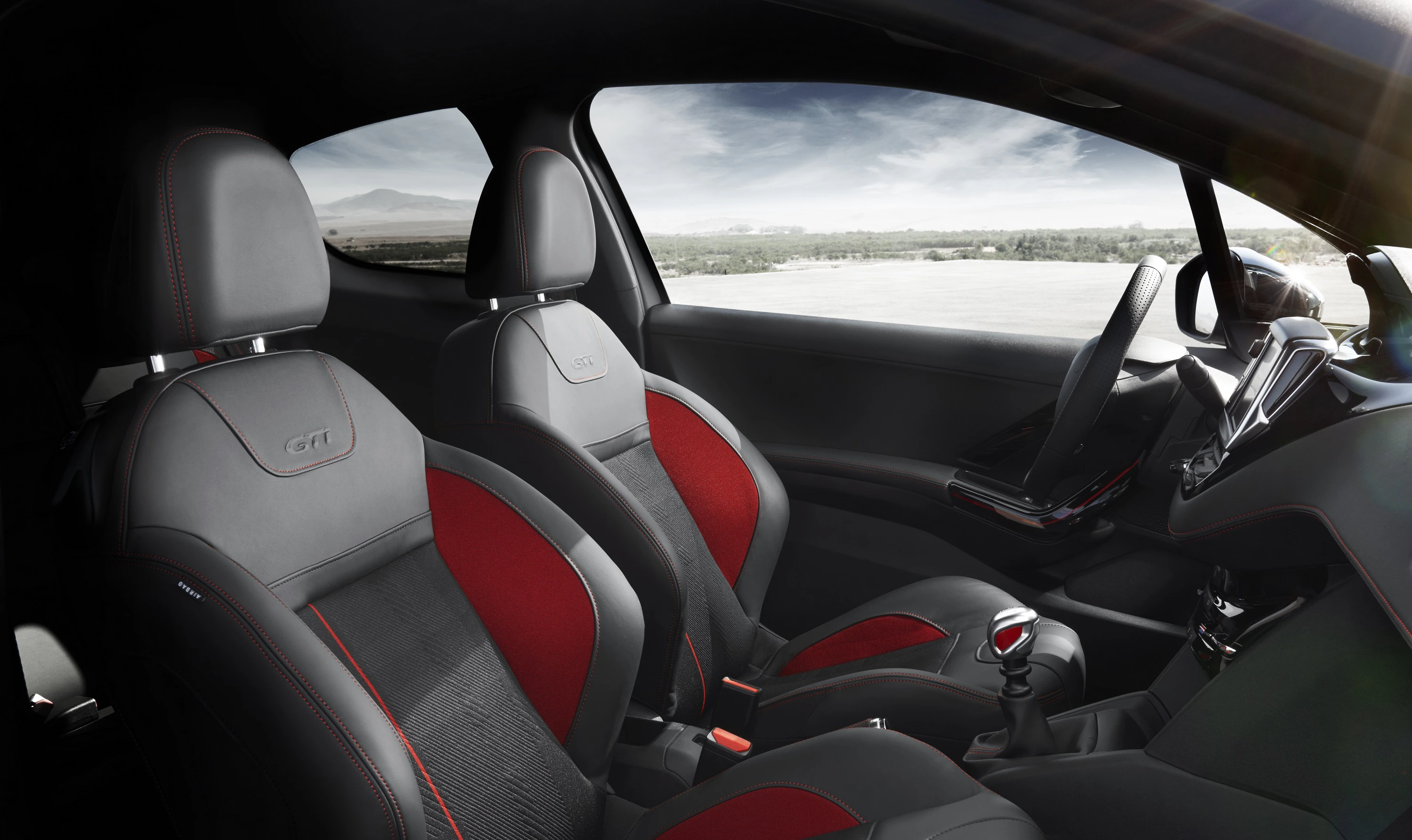 Innenraum eines modernen Autos mit grauen und roten Sportsitzen, schwarzem Armaturenbrett und weitem Blick auf die Landschaft durch die Windschutzscheibe.