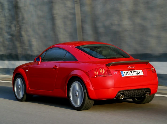 Roter Audi TT fährt auf einer Straße entlang einer Mauer, Hinteransicht, sportliches Design, glänzende Oberfläche, schnelle Bewegung.