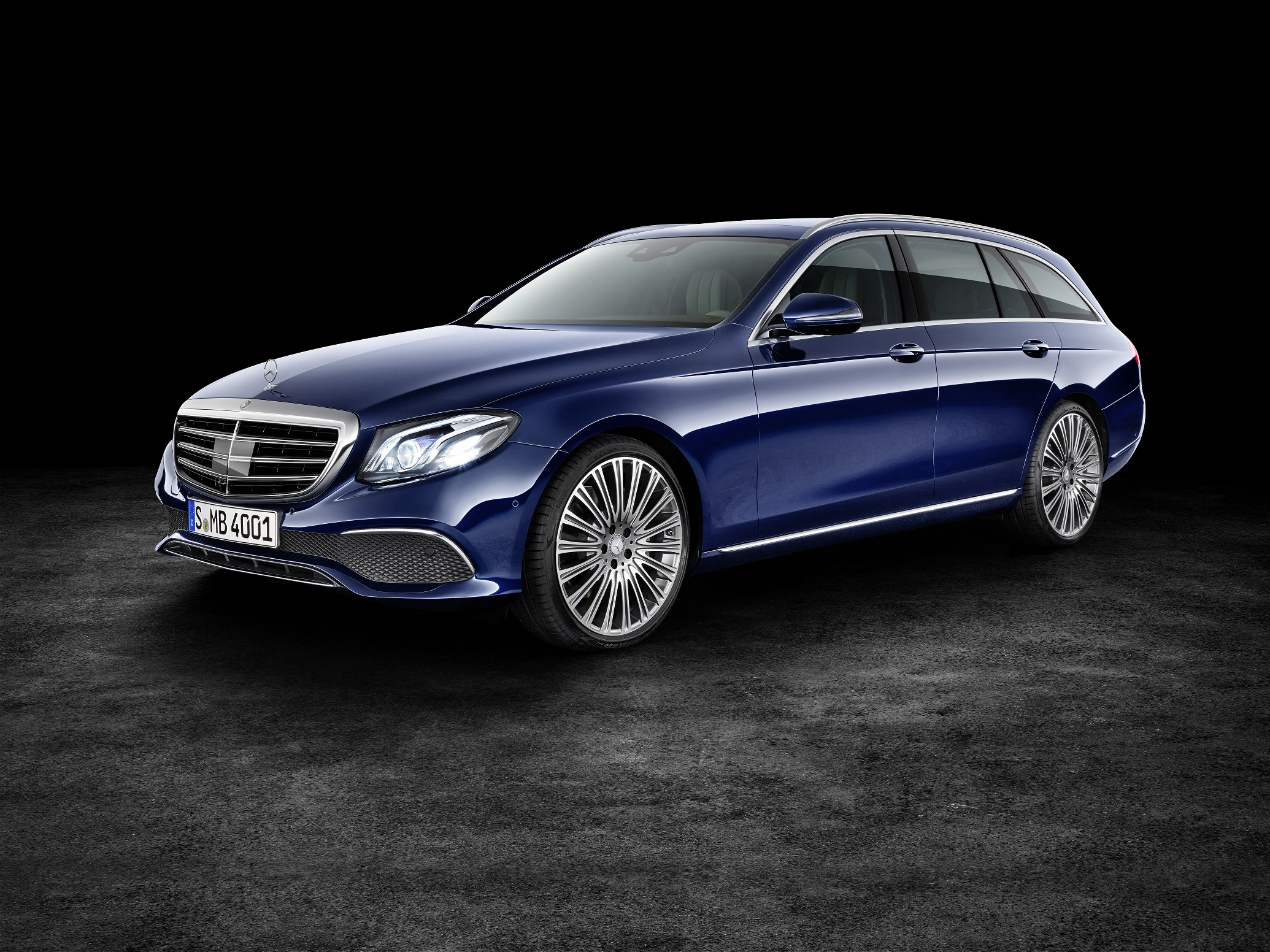 Blauer Mercedes-Benz Kombi vor schwarzem Hintergrund, seitliche Ansicht, moderne Scheinwerfer und markante Felgen.
