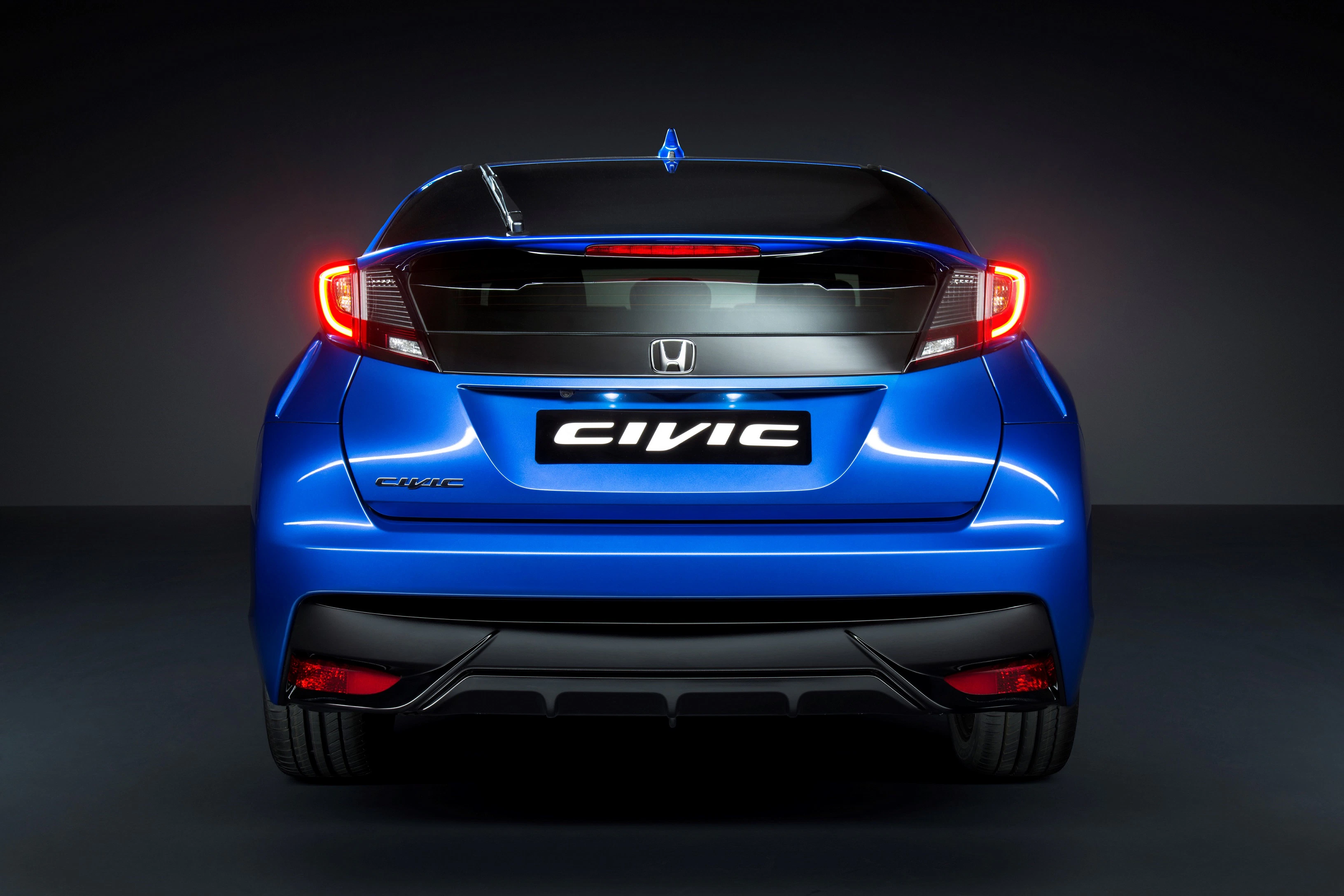Blauer Honda Civic von hinten, mit leuchtenden Rücklichtern und markantem Heckdesign vor dunklem Hintergrund.