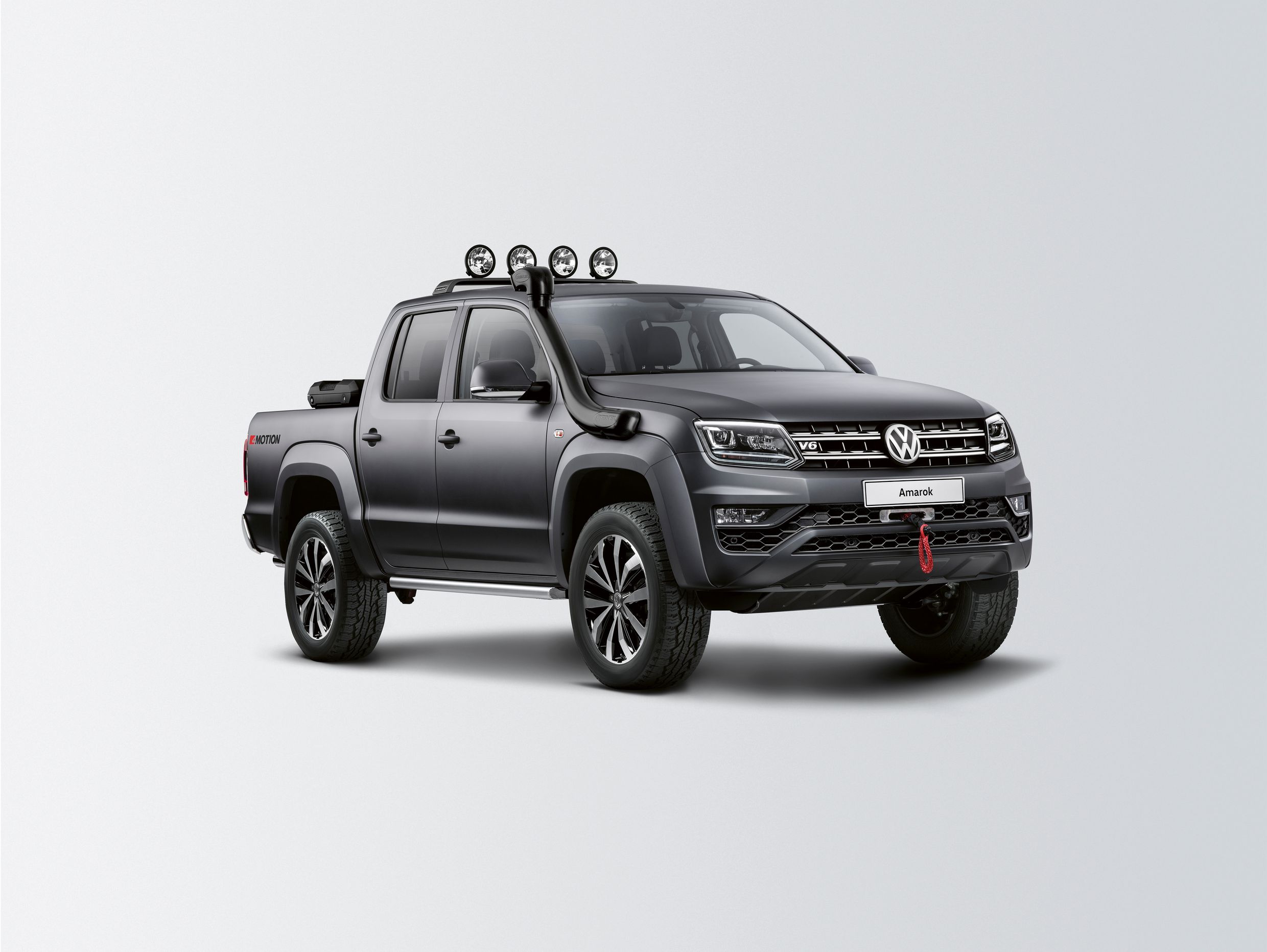 Ein grauer Volkswagen Amarok Pickup mit Offroad-Reifen und Zusatzscheinwerfern auf hellem Hintergrund.