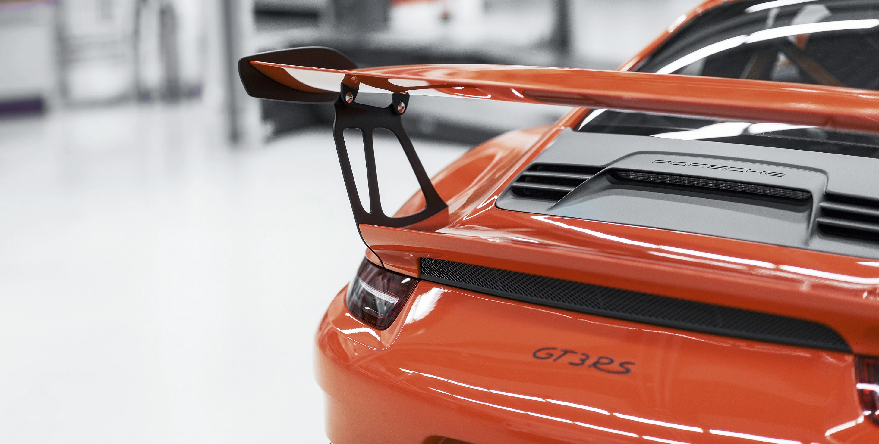 Nahaufnahme eines orangefarbenen Sportwagens mit großem Heckspoiler und dem Schriftzug „GT3 RS“ am Heck. Hintergrund unscharf.