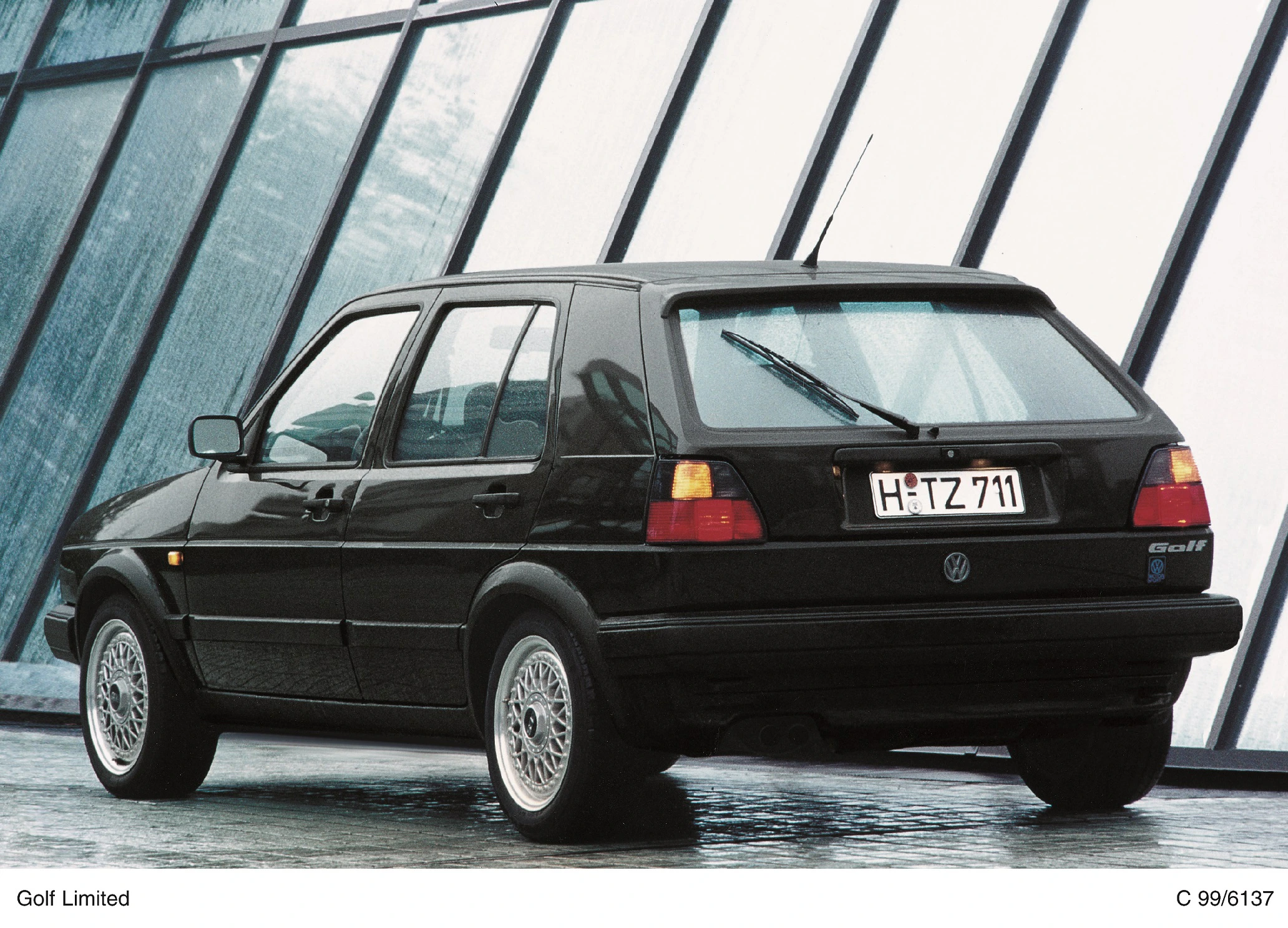 Schwarzer VW Golf Limited vor moderner Glasarchitektur, von hinten fotografiert. Fahrzeugdetails wie Rücklichter und Felgen gut sichtbar.