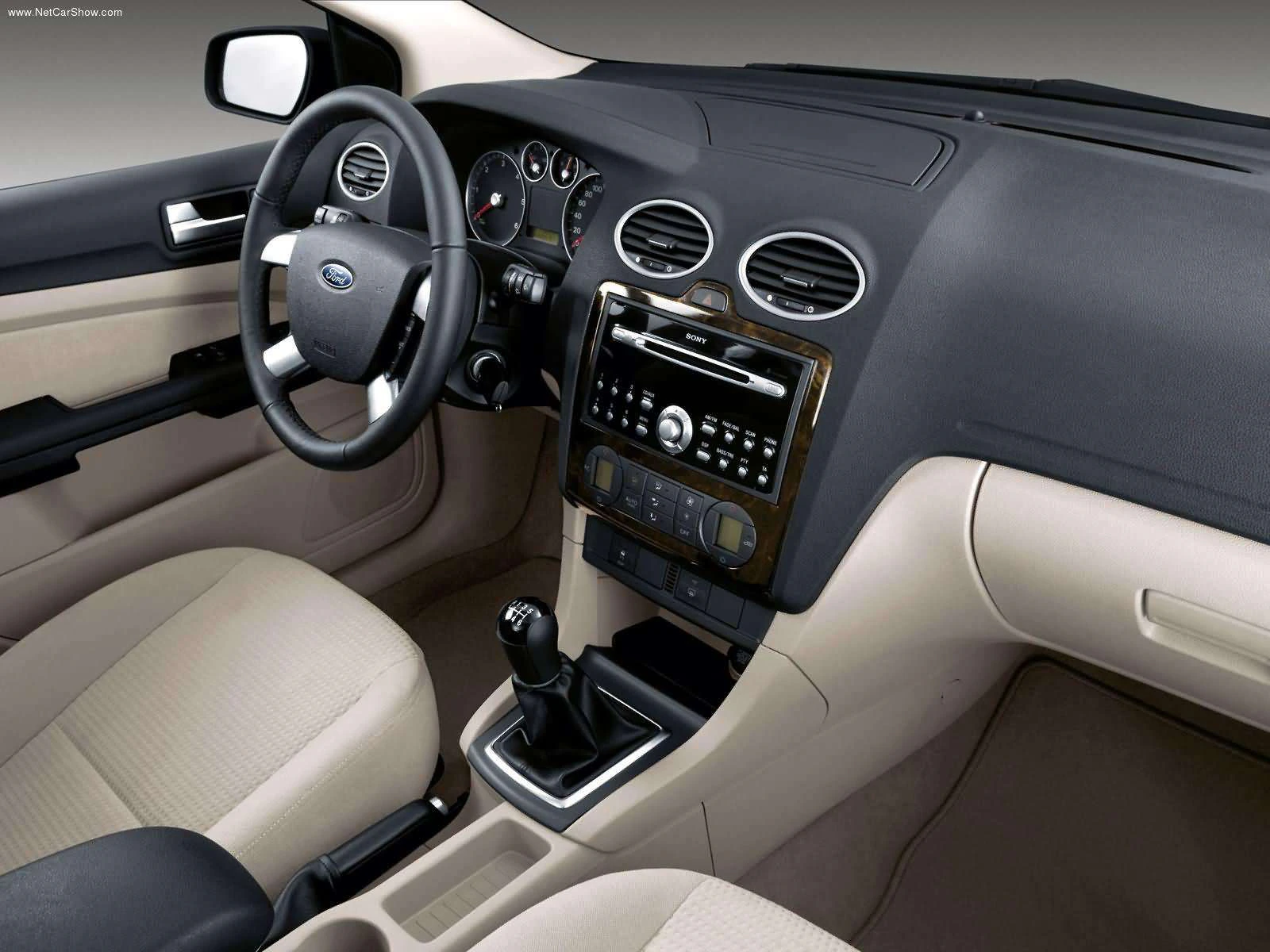 Innenraum eines Autos mit Lenkrad, Schalthebel, Armaturenbrett mit Bedienelementen und beigen Sitzen. Modernes Design, zentrale Konsole gut sichtbar.