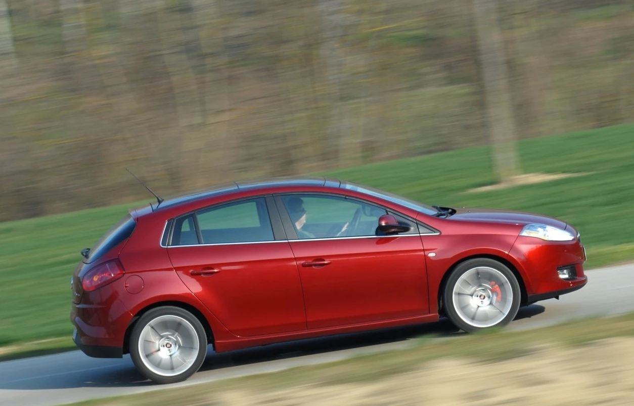 Roter Kleinwagen fährt schnell auf einer Straße, umgeben von grüner Landschaft und unscharfem Hintergrund.