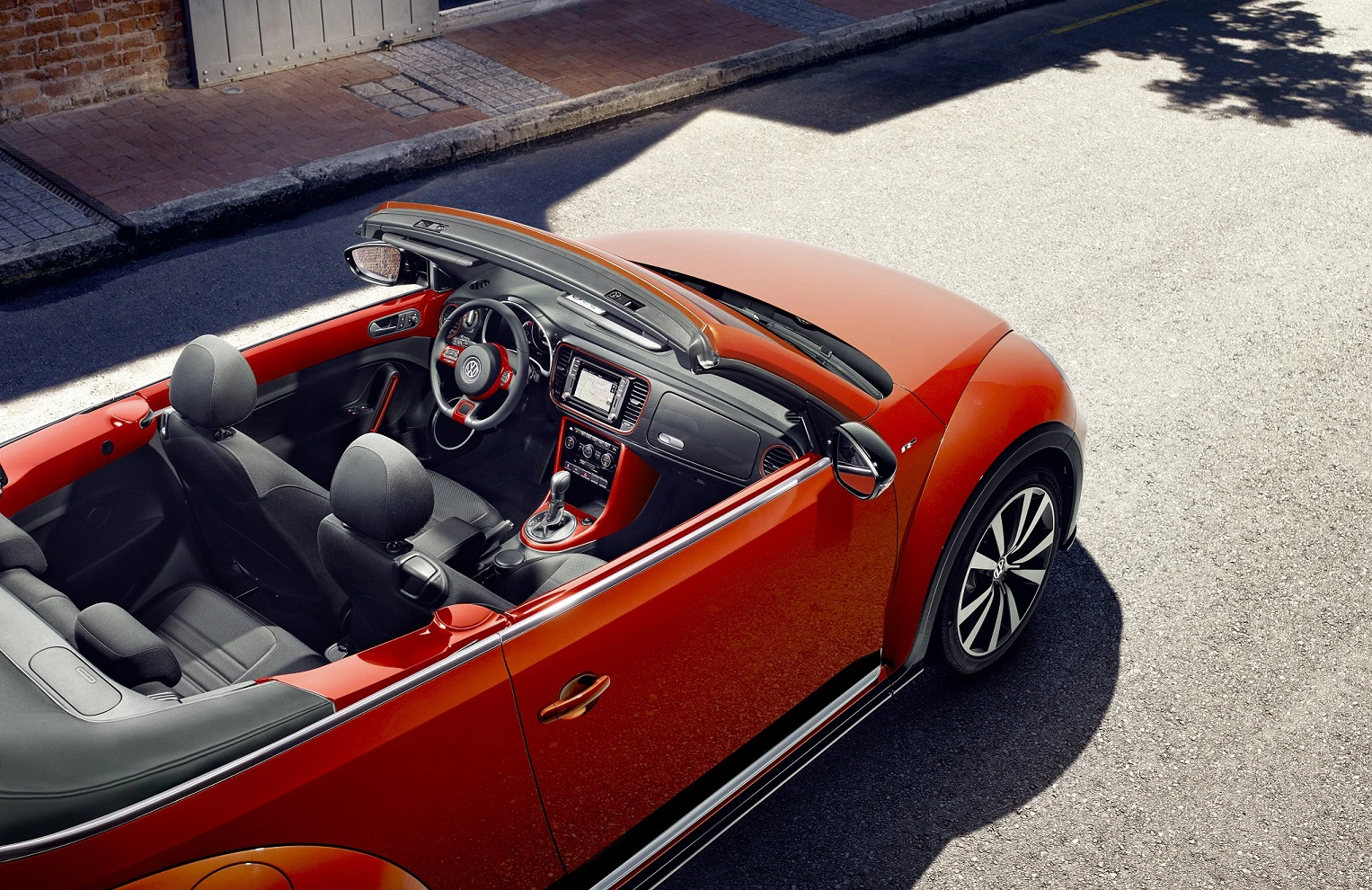 Rotes Cabriolet steht offen auf einer sonnigen Straße. Sicht von oben zeigt Lenkrad, Armaturenbrett und Vordersitze.