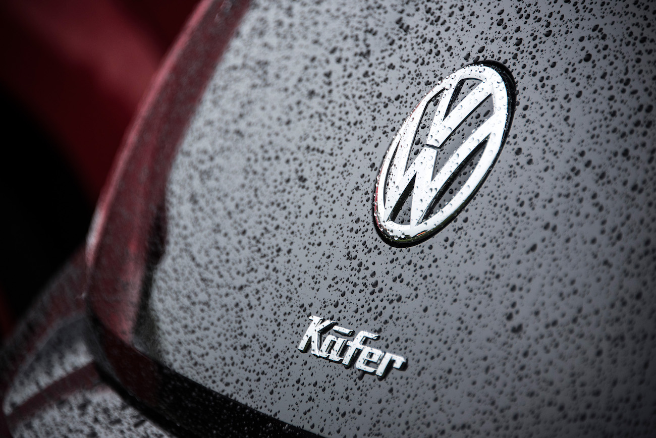 Nahaufnahme eines VW Käfer-Logos auf einem regennassen Autolack.