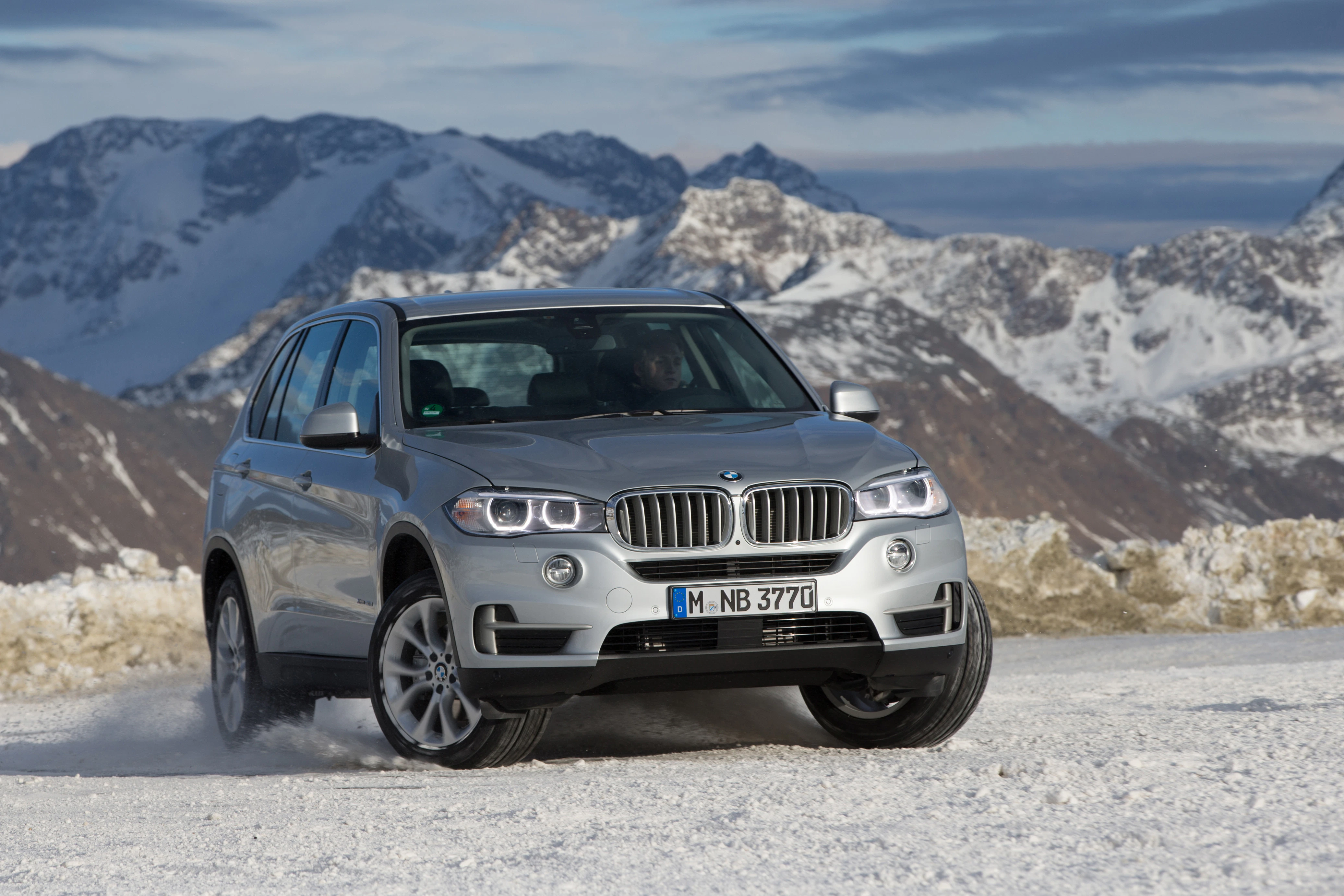 Ein silberner BMW-SUV fährt auf verschneiter Straße vor einer malerischen Bergkulisse.