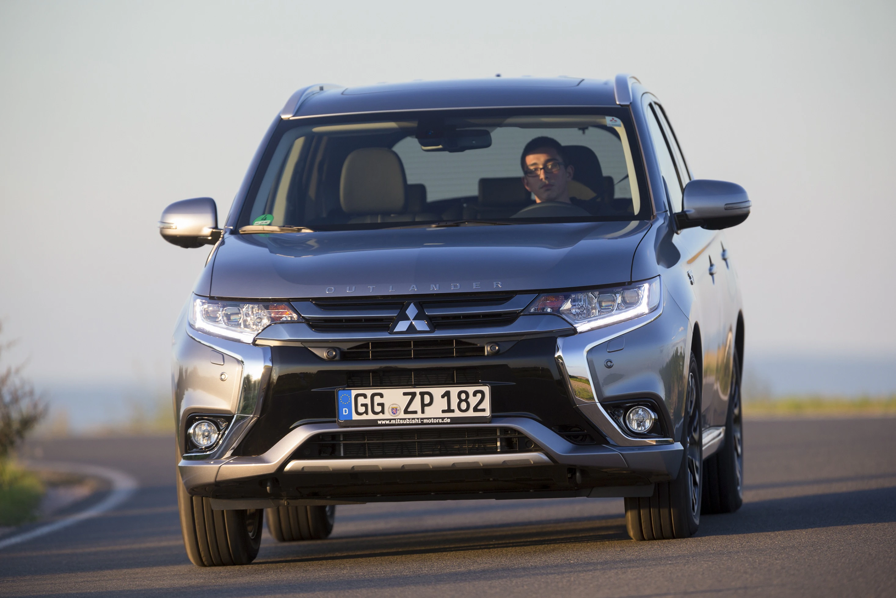 Ein grauer Mitsubishi Outlander fährt auf einer Straße, der Fahrer sitzt konzentriert hinter dem Steuer.