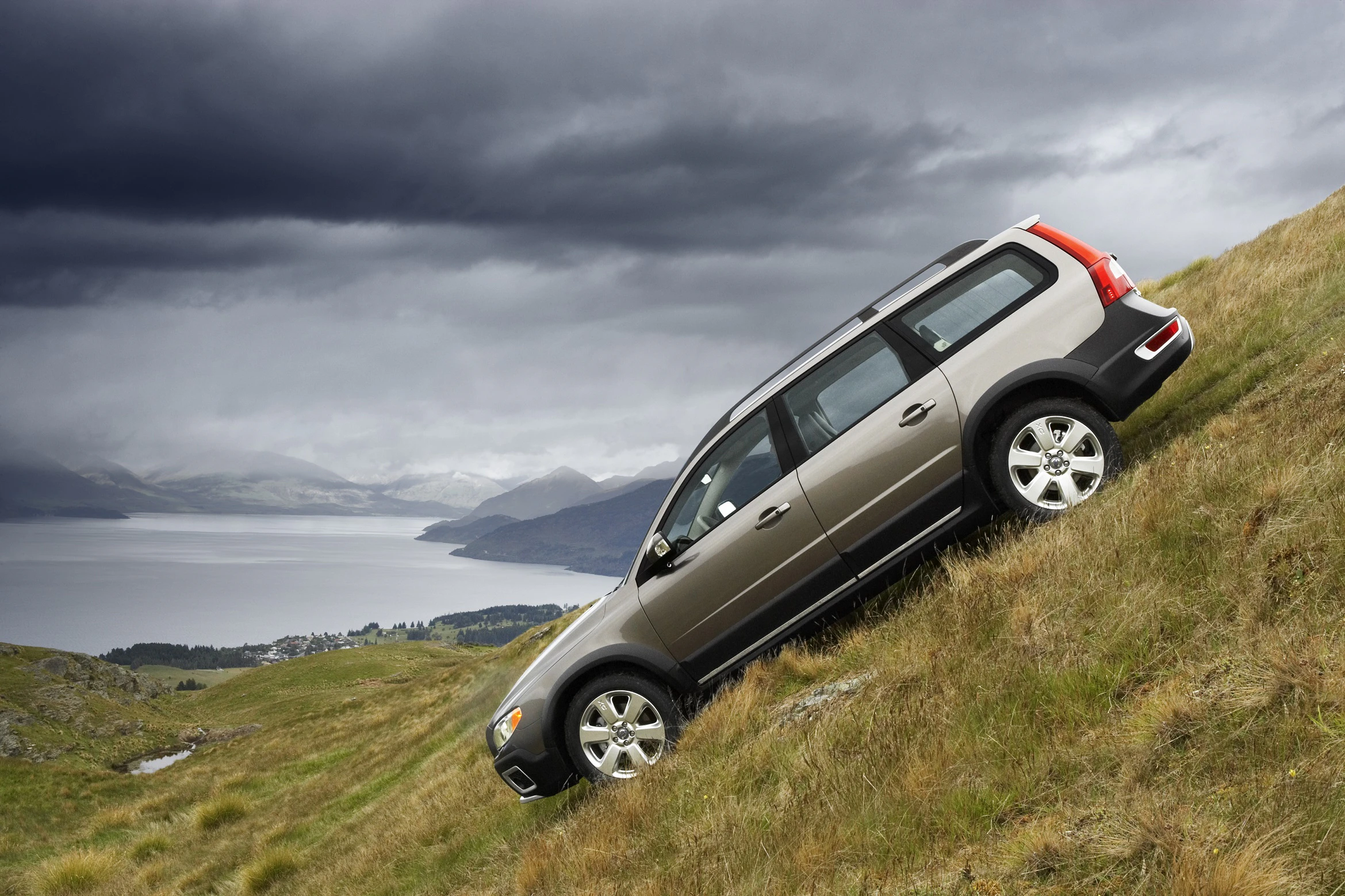 SUV fährt einen steilen, grasbewachsenen Hang hinauf. Im Hintergrund bewölkter Himmel und ein Blick auf Wasser und Hügel.