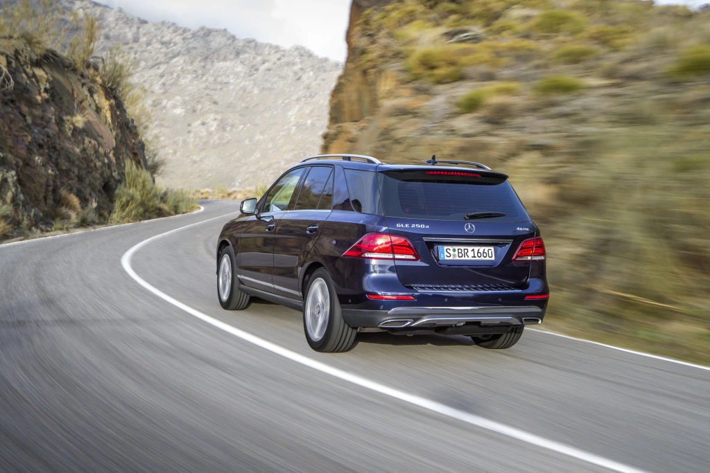 Schwarzer SUV fährt auf kurviger Bergstraße; steile Felsen und spärliche Vegetation im Hintergrund.