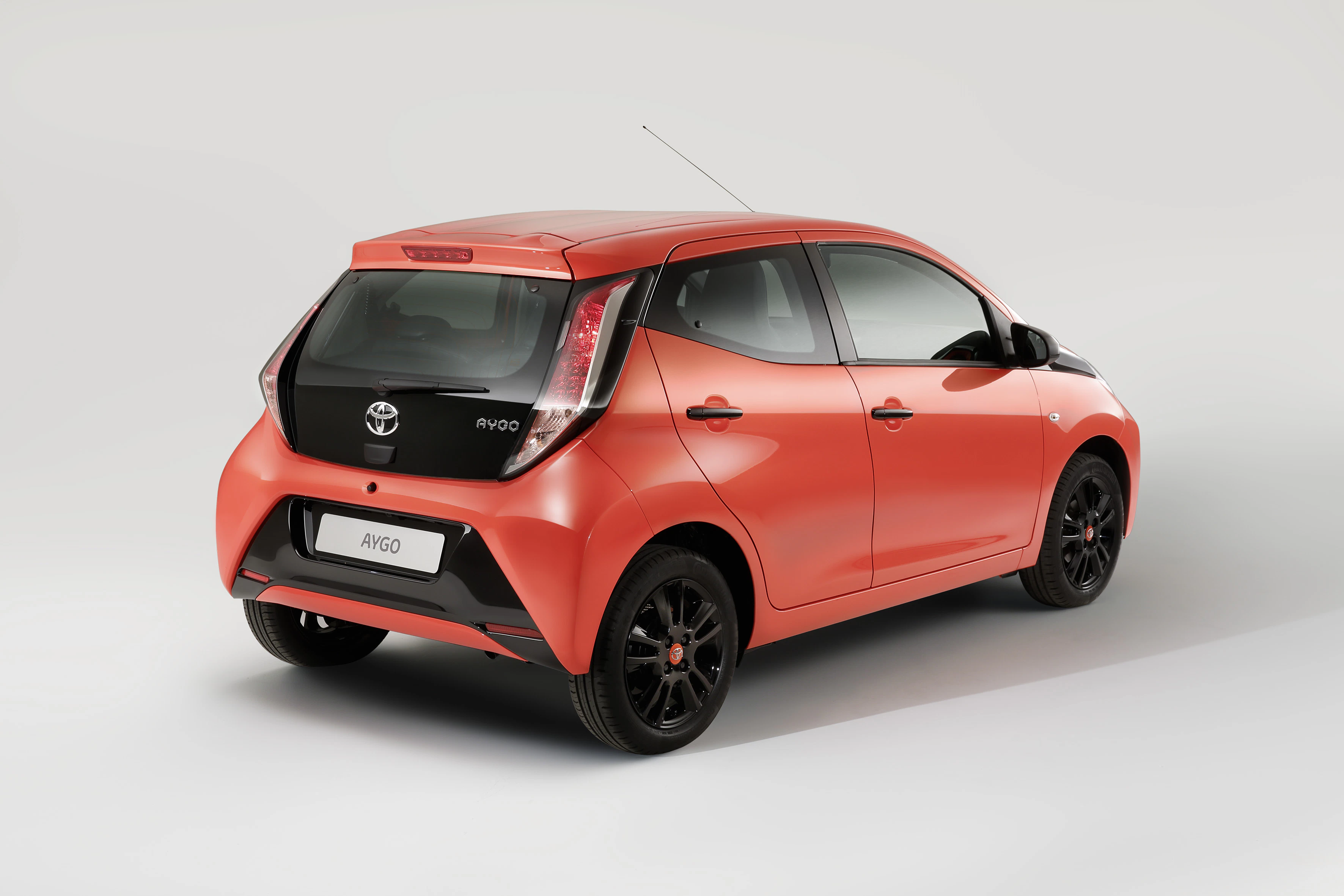 Roter Toyota Aygo von hinten rechts, vor grauem Hintergrund. Fahrzeug hat schwarze Felgen und modern gestaltete Rücklichter.