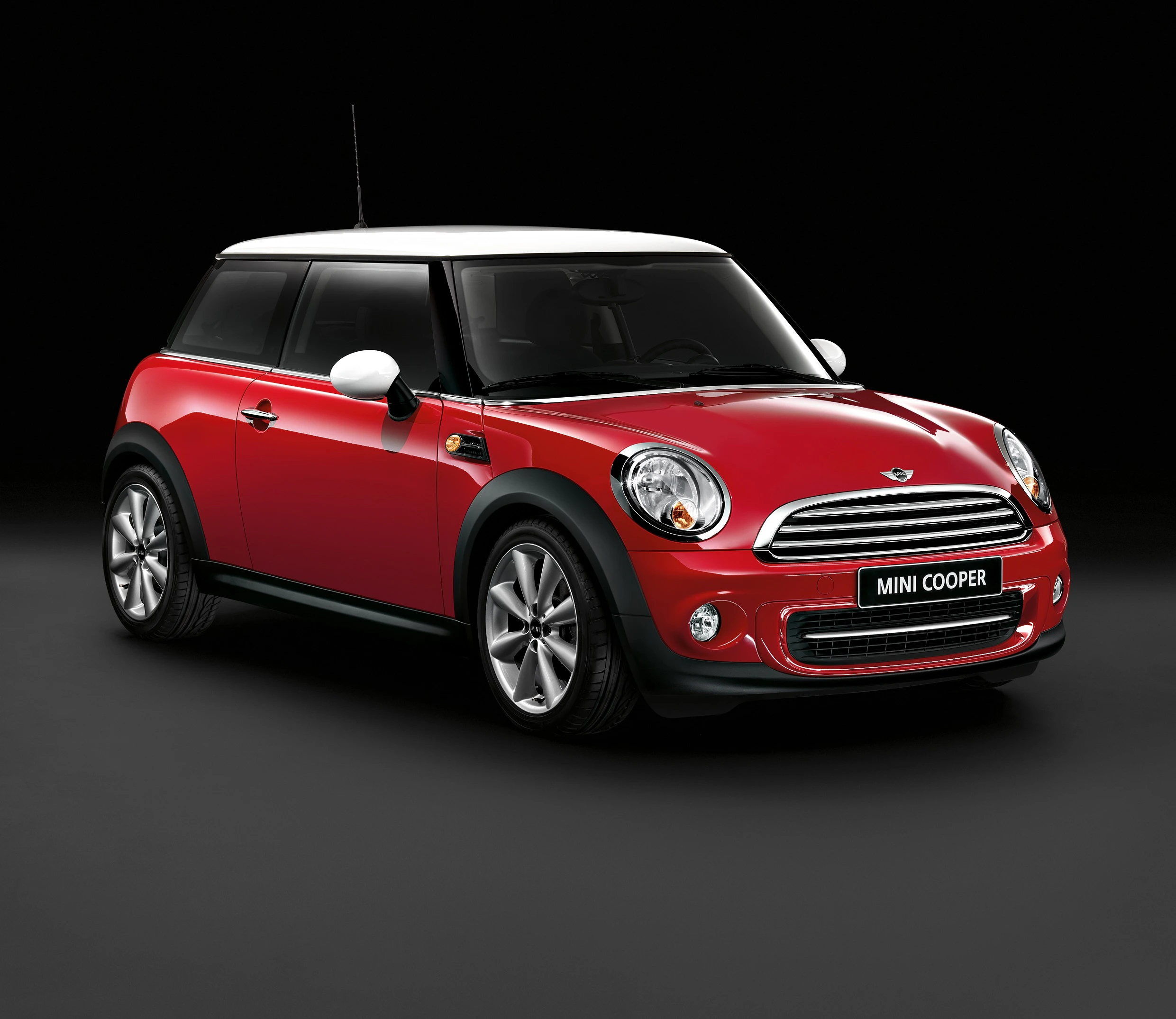 Roter Mini Cooper mit weißem Dach und Spiegeln vor schwarzem Hintergrund, schräg von vorne fotografiert.