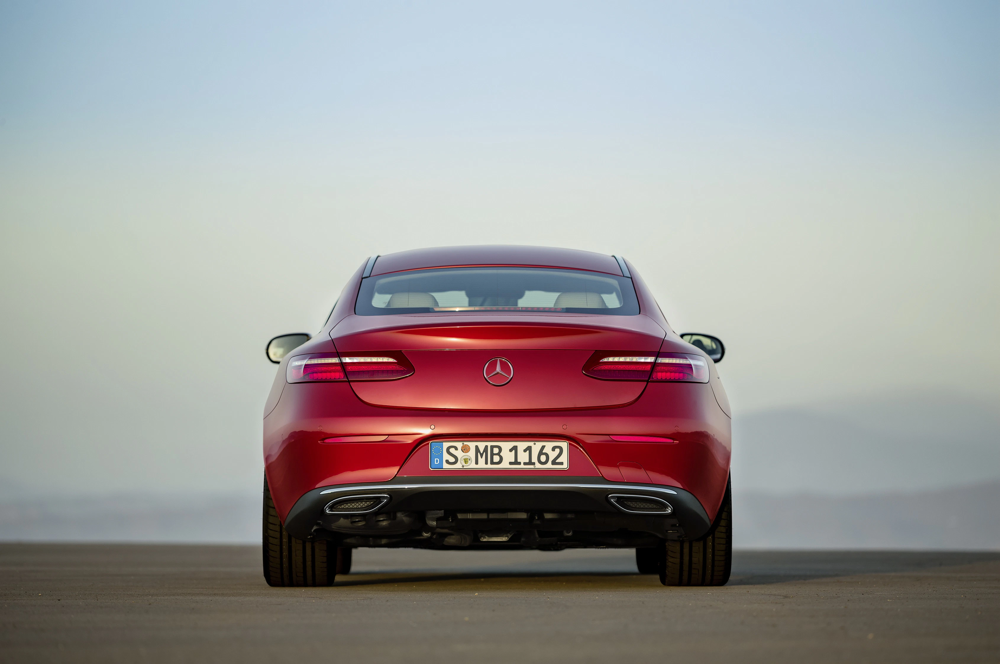 Rotes Mercedes-Benz Coupé von hinten, auf einer leeren Straße geparkt, mit leichtem Nebel im Hintergrund.