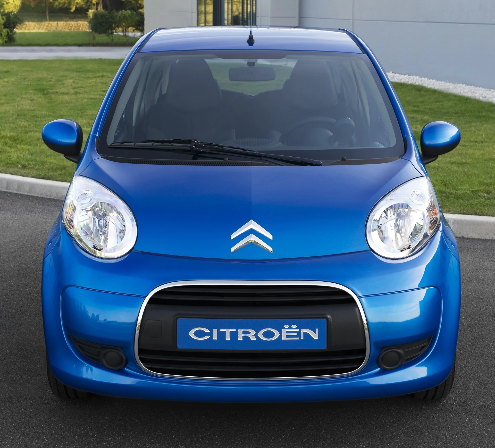 Blauer Citroën Kleinwagen von vorne, auf einer Straße geparkt, mit modernem Design und grünem Rasen im Hintergrund.