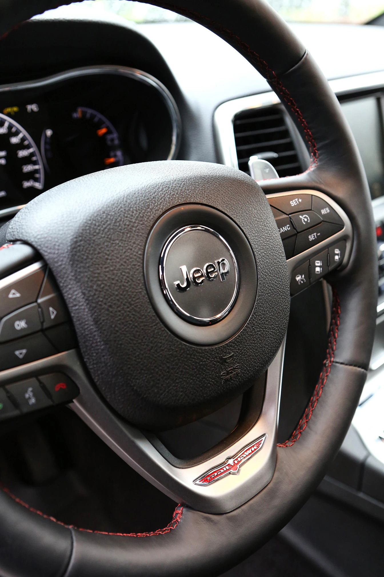 Nahaufnahme eines Jeep-Lenkrads mit Bedienelementen für Radio und Tempomat. Instrumententafel im Hintergrund teilweise sichtbar.