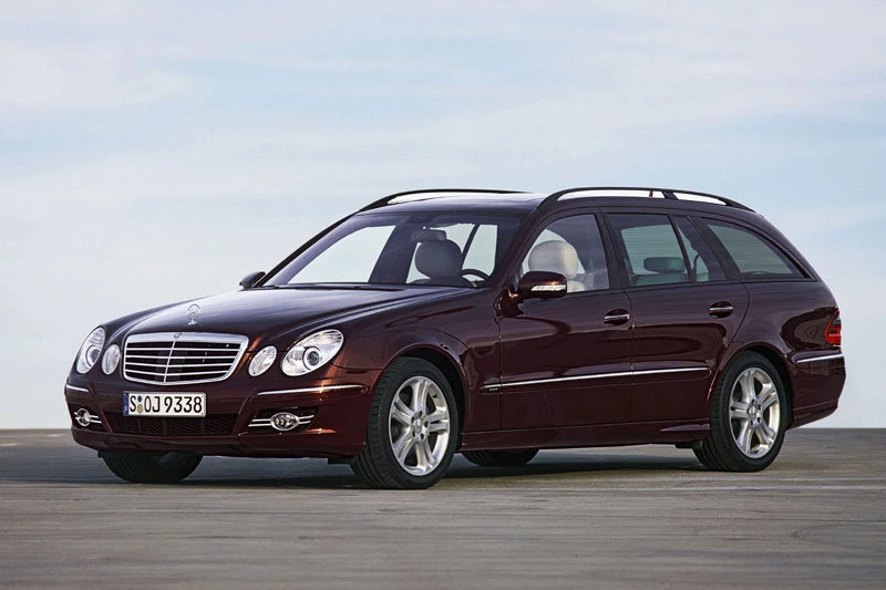Bordeauxroter Kombi Mercedes E-Klasse (W211) auf leerer Straße bei blauem Himmel, seitliche Ansicht.