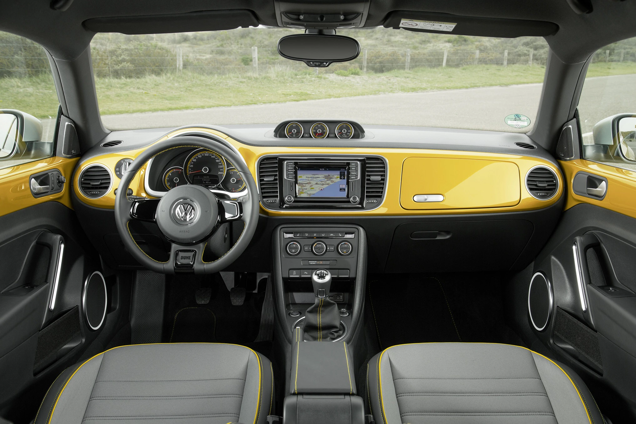 Innenraum eines gelben VW-Beetles mit schwarzer und grauer Lederausstattung, modernem Armaturenbrett und rundem Lenkrad.