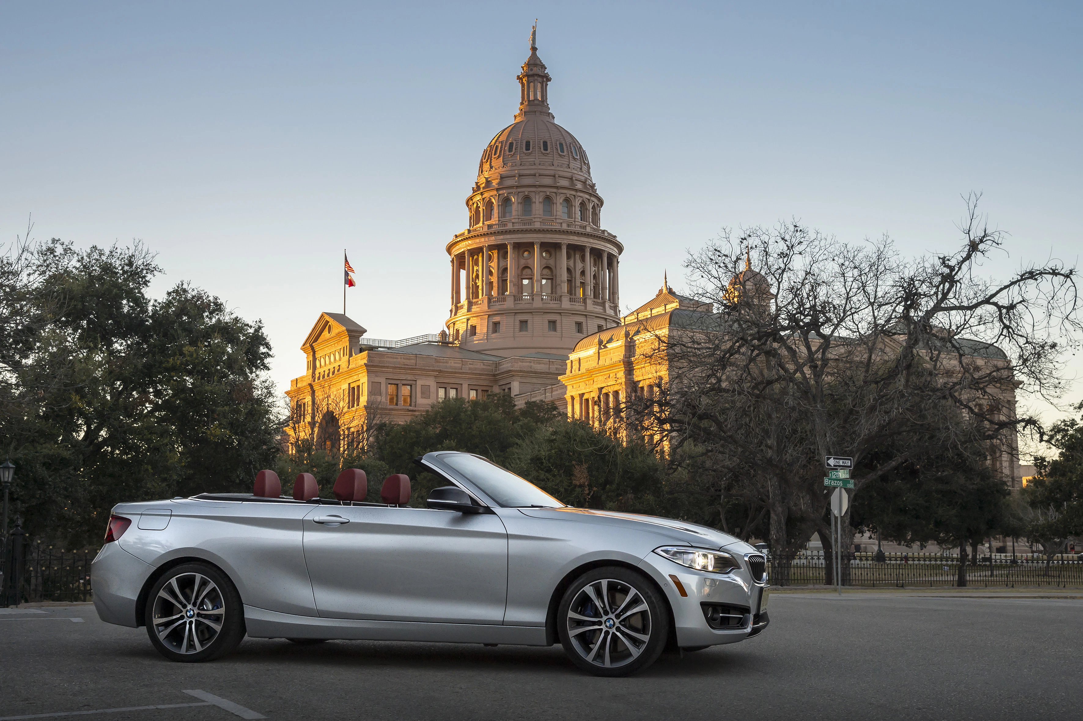 Silbernes Cabrio vor dem Kapitol in Austin, Texas, bei Sonnenuntergang. Das Gebäude strahlt in warmem Licht, klare Himmel im Hintergrund.