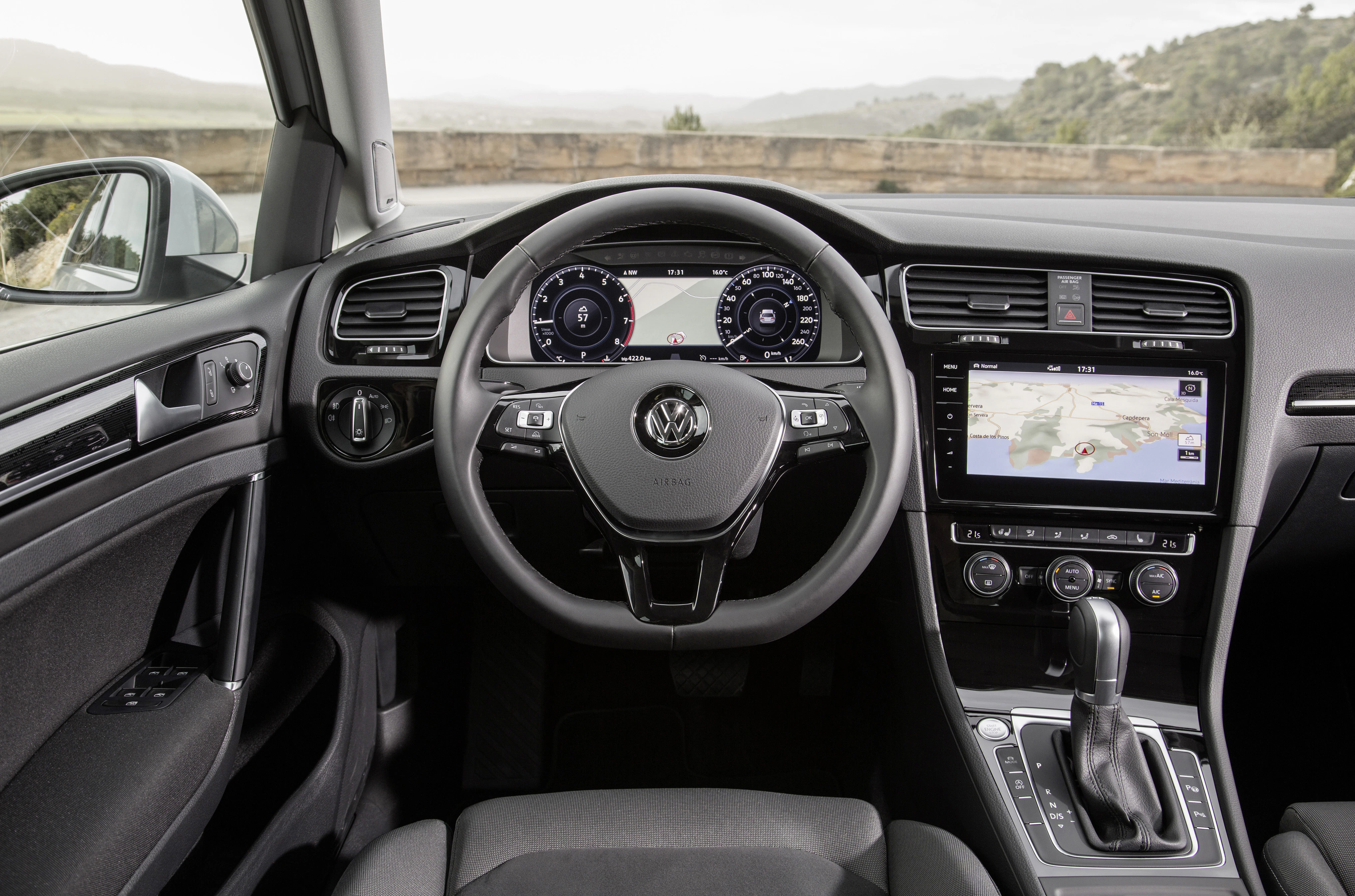 Innenansicht eines Autos mit modernem Armaturenbrett, Touchscreen-Navigation und Multifunktionslenkrad vor einer Landschaft.
