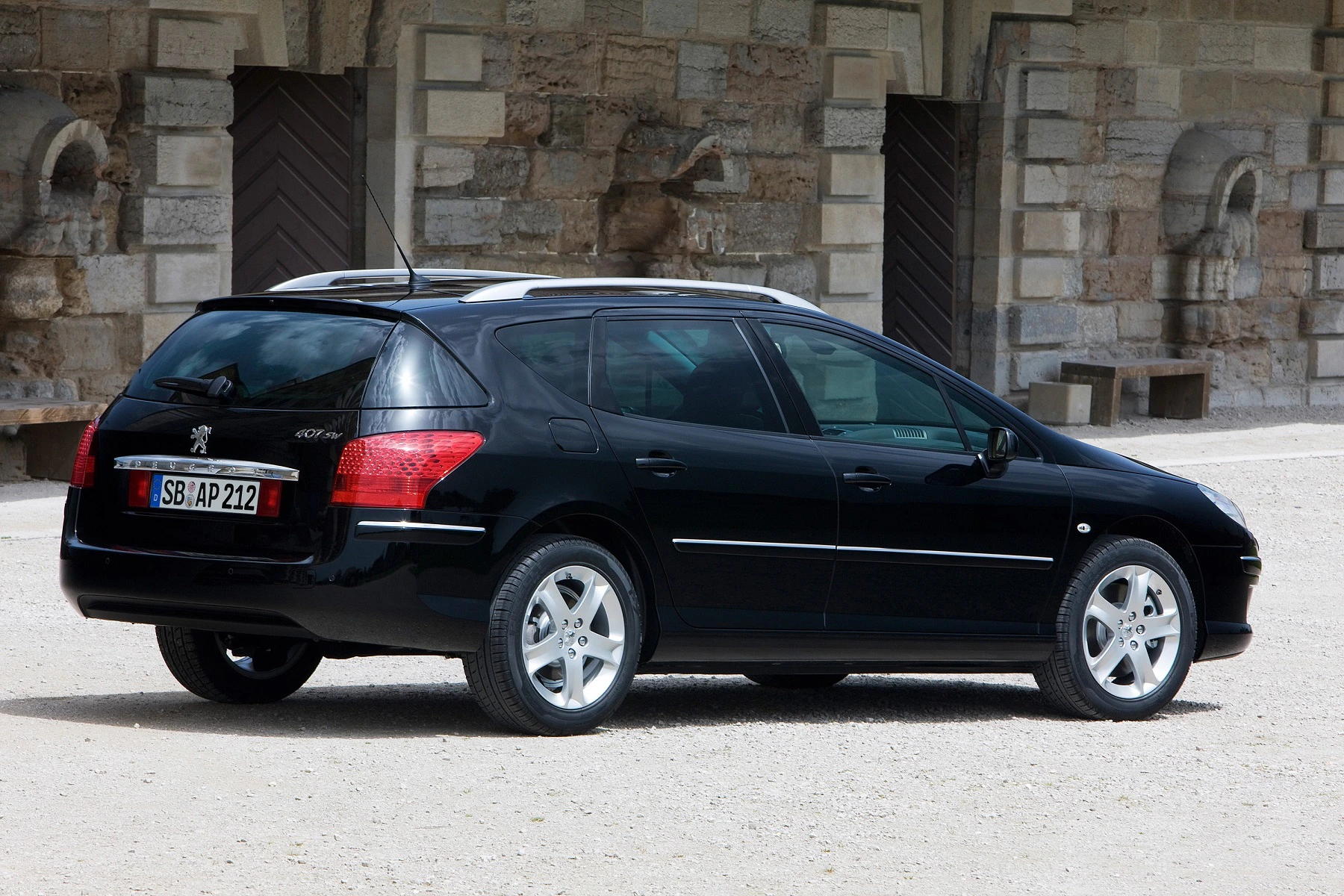 Schwarzer Peugeot 407 Kombi steht im Freien vor einer Steinmauer. Das Auto hat silberne Felgen und eine Dachreling.