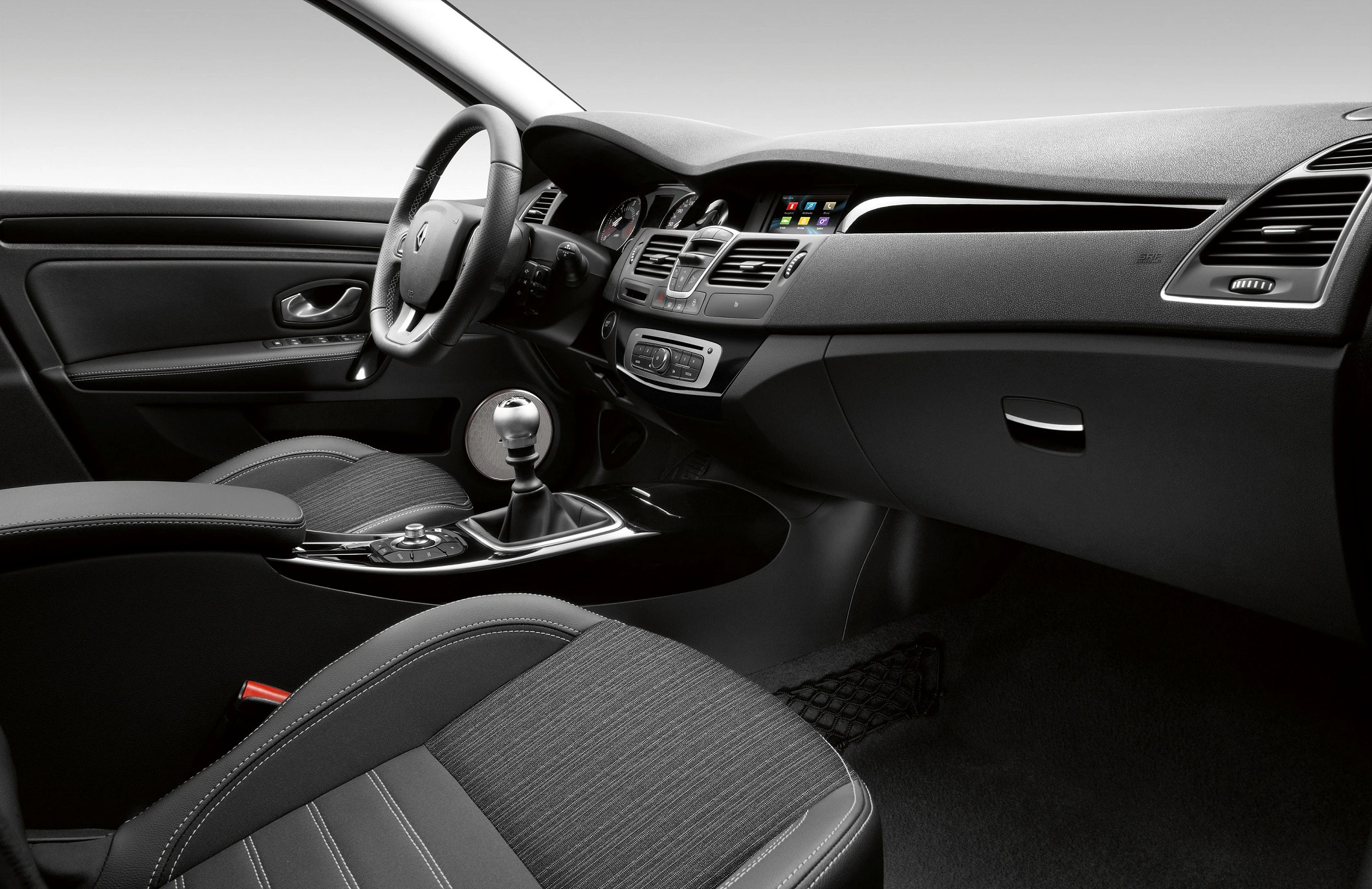 Innenraum eines Autos mit schwarzen Sitzen, Lenkrad, Schalthebel und einem modernen Armaturenbrett mit Display und Bedienelementen.
