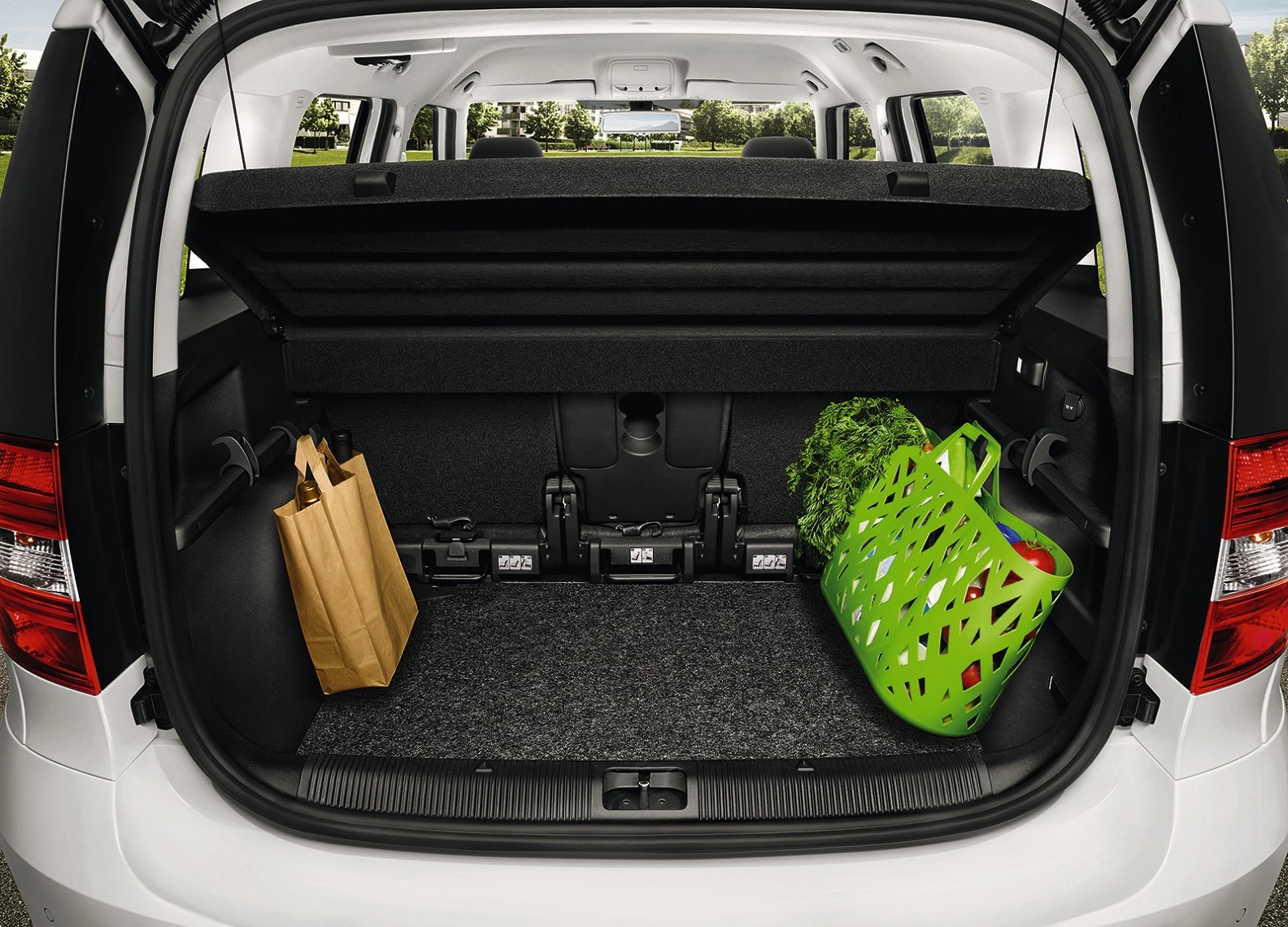 Kofferraum eines Autos mit einem Papierbeutel links und einem grünen Korb mit frischen Kräutern rechts.