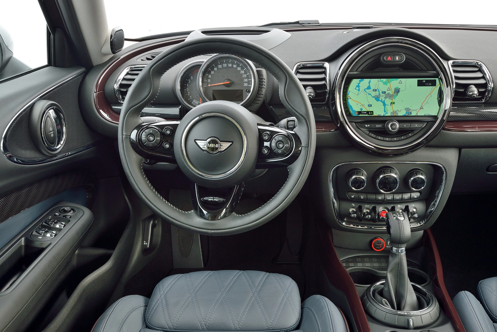 Innenraum eines Autos mit Lenkrad, Tachometer und zentralem Touchscreen-Navigationssystem, Ledersitze und manueller Schaltknüppel.